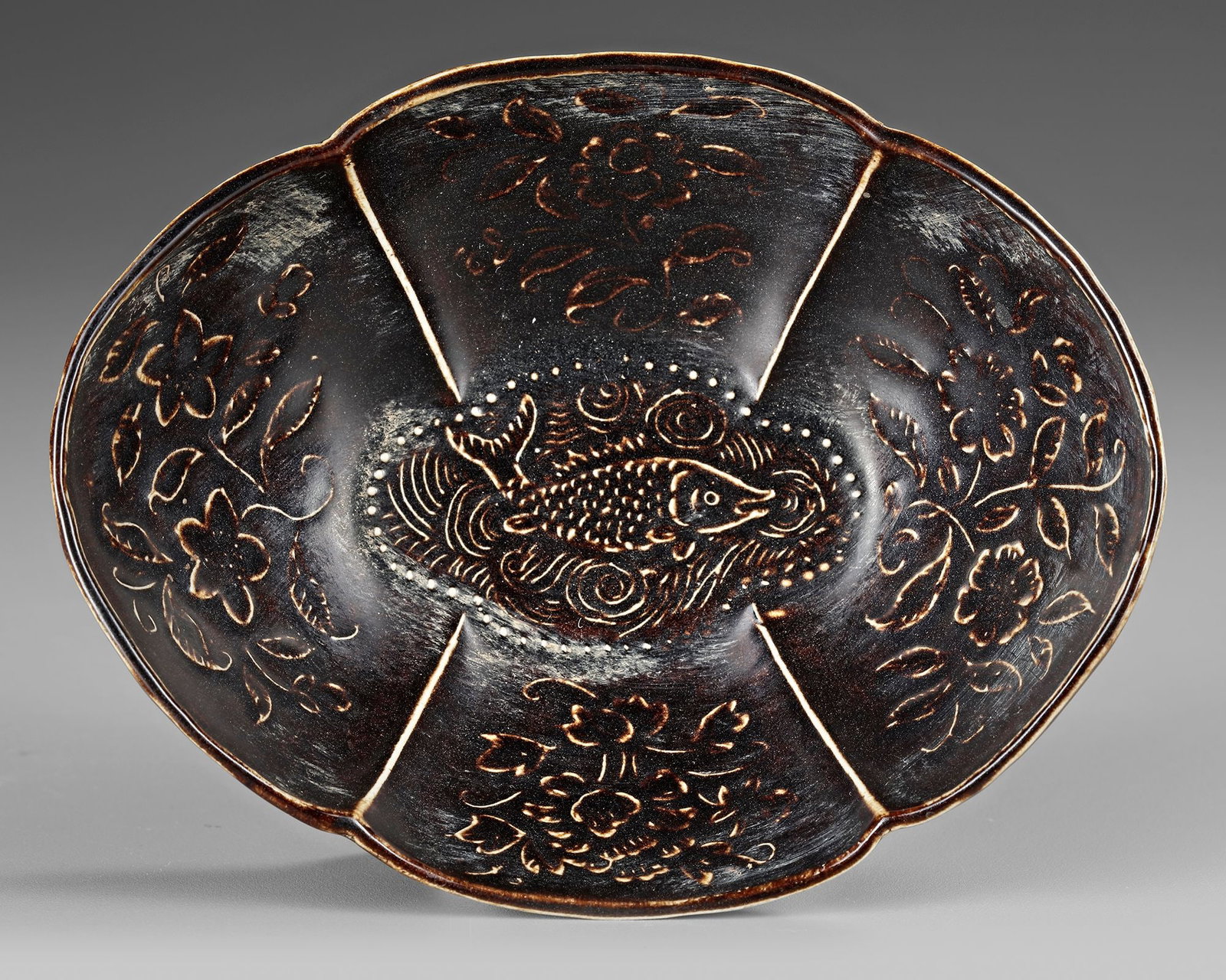 A CHINESE CIZHOU-TYPE BLACK-GLAZED INCISED FOLIATE BOWL, SONG DYNASTY (960-1279): Finely potted as a lobed foliate bowl raised on a short oval foot, the vessel is covered in a lustrous dark brownish-black glaze and delicately incised through the glaze to reveal the pale body beneat