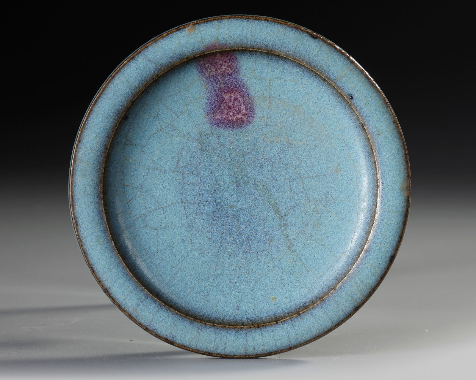 A CHINESE JUNYAO PURPLE-SPLASHED SAUCER DISH, YUAN DYNASTY (1279-1368): A Chinese dish with rounded sides and an everted rim, covered overall with a mottled milky-blue glaze that thins to dark mushroom at the rim and includes one bluish-purple splash on the interior. The 
