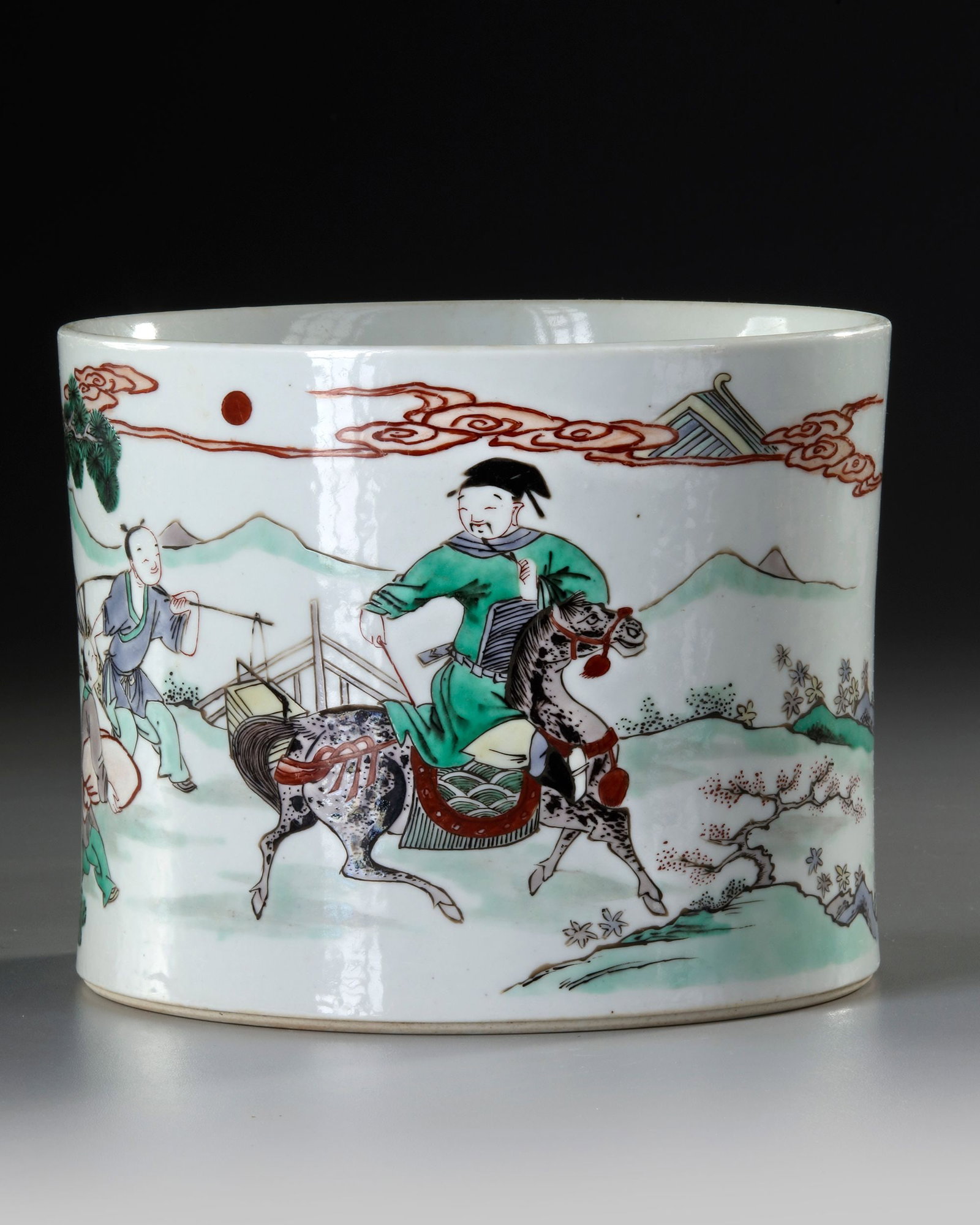 A CHINESE FAMILLE VERTE BRUSH POT, QING DYNASTY (1644-1911): A Chinese porcelain brush pot decorated in famille verse enamels with a horseman accompanied by two servants under a pine tree in a landscape. 15.5 by 19.5 cm.