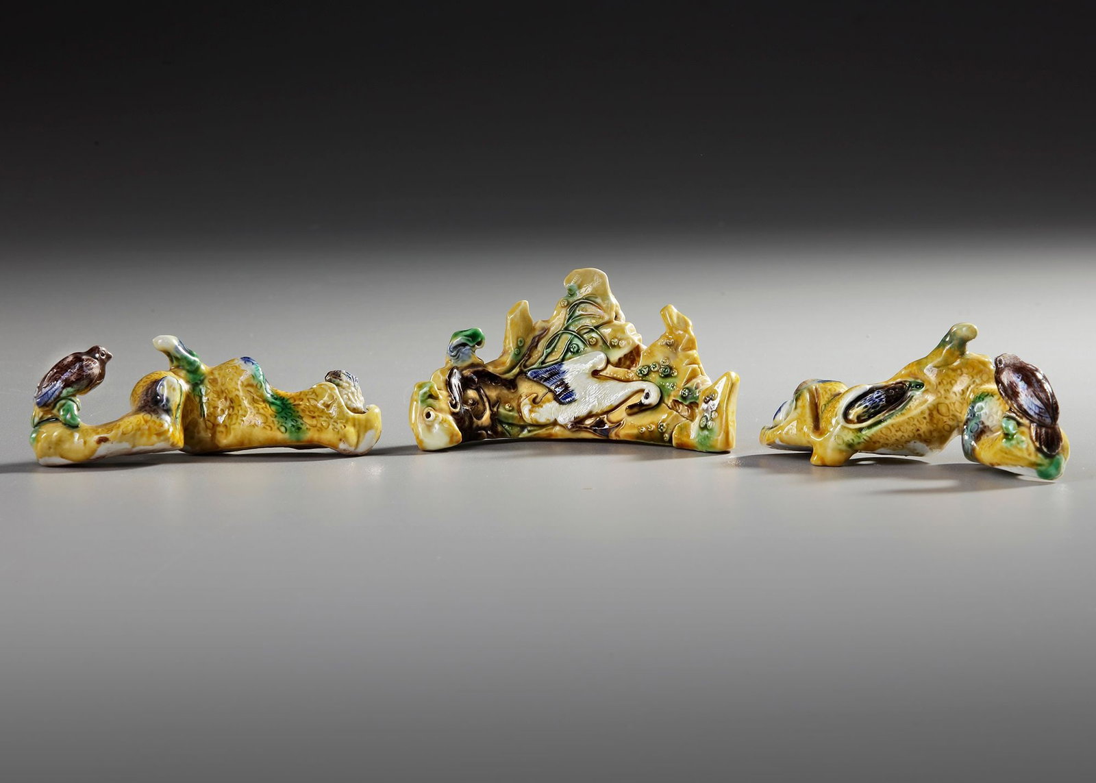 THREE CHINESE BISCUIT BRUSH RESTS, 18TH CENTURY: The central biscuit rock-molded brush rest is decorated with a white-glazed duck in low relief, the other two brush rests are molded as tree branches with a bird perched in high relief. Length 9-10-11