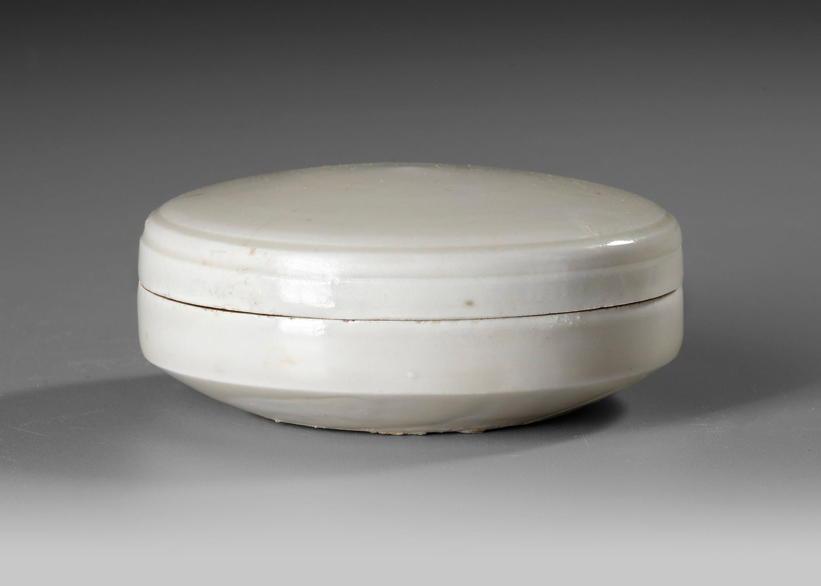A CHINESE 'DING' BOX AND COVER, NORTHERN SONG DYNASTY: A Chinese porcelain box with straight sides tapering in towards the base and a domed cover, applied overall with an ivory-tinged glaze with characteristic teardrops on the sides. Diam : 9 cm. Height: 