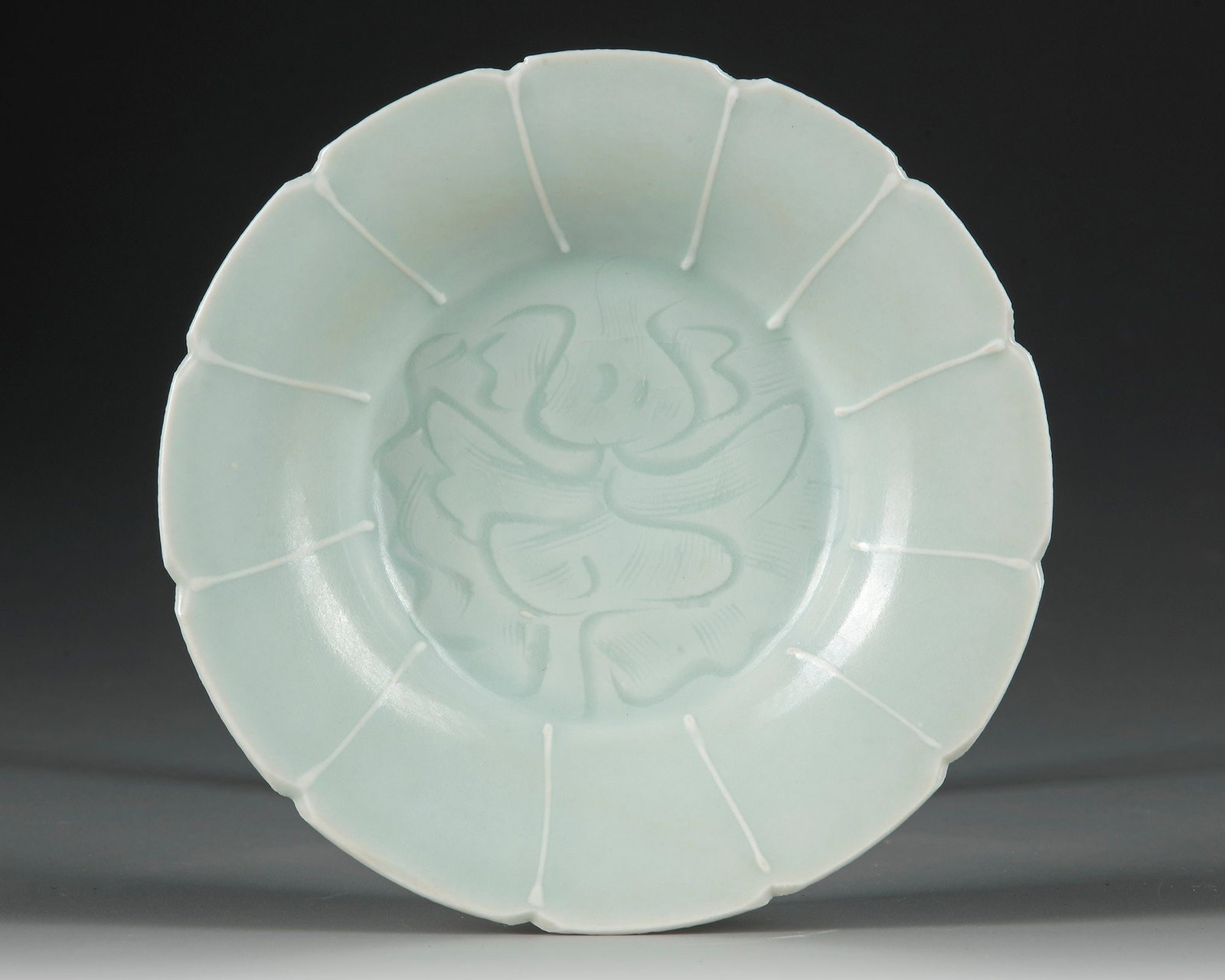 A CHINESE QINGBAI LOBED 'FLORAL' DISH,SONG DYNASTY (960-1279 AD): Thinly potted, the bowl has gently flaring sides with narrow ribs rising to a petal-lobed rim. It is covered overall with a thin glaze of pale blue tone, falling to the edge of the unglazed base. Diam