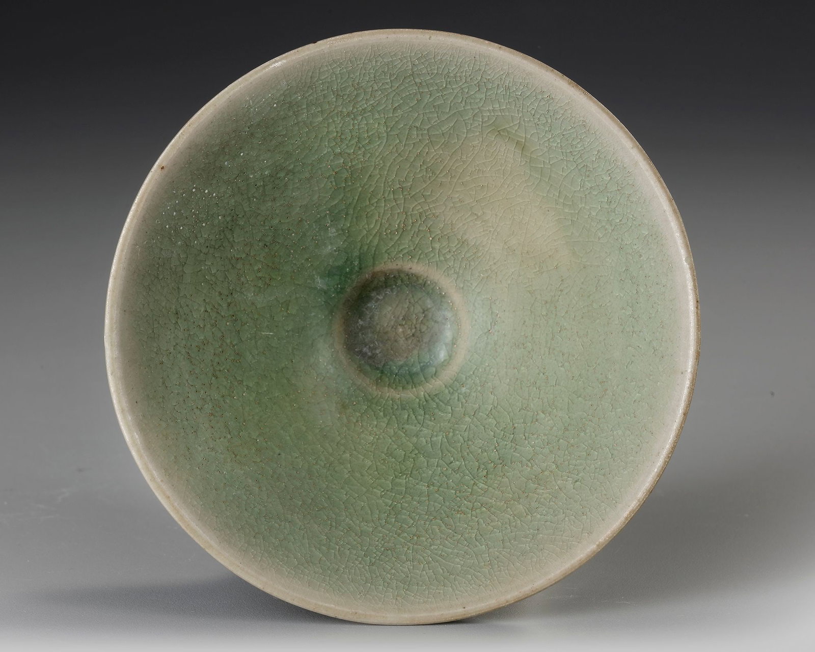 A CHINESE CELADON GLAZED BOWL,MING DYNASTY (1368-1644): A finely potted, shallow conical bowl rising from a small, neatly trimmed foot ring, covered overall in a pale green celadon glaze with finely crackled surface. The glaze deepens to darker green and b