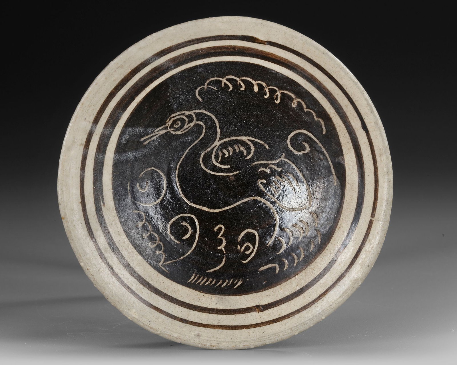 A CHINESE CIZHOU SGRAFFIATO BOWL WITH BIRD DECORATION, SONG DYNASTY OR LATER: A finely potted shallow bowl with a broad, slightly everted rim and low ring foot, covered overall with a creamy white slip beneath a transparent glaze. The interior is boldly decorated with a dark br