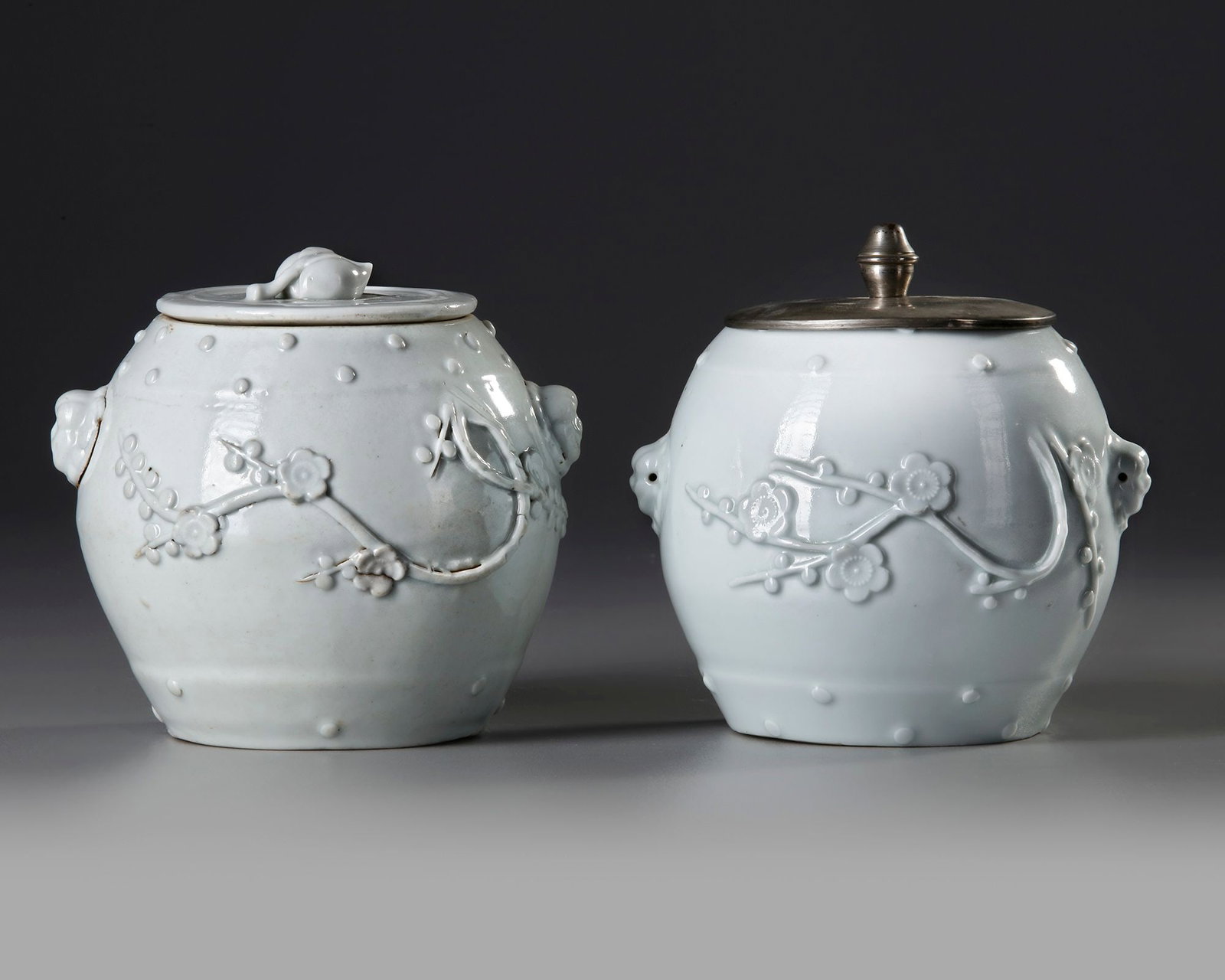 TWO CHINESE BLANC DE CHINE BARREL SHAPED JARS AND A COVER, 18TH CENTURY: The flattened circular lid with twin peach finial, the curving sides of the jar decorated with bands of raised dot designs at the rim and base, the sides otherwise decorated with blossom sprays in low