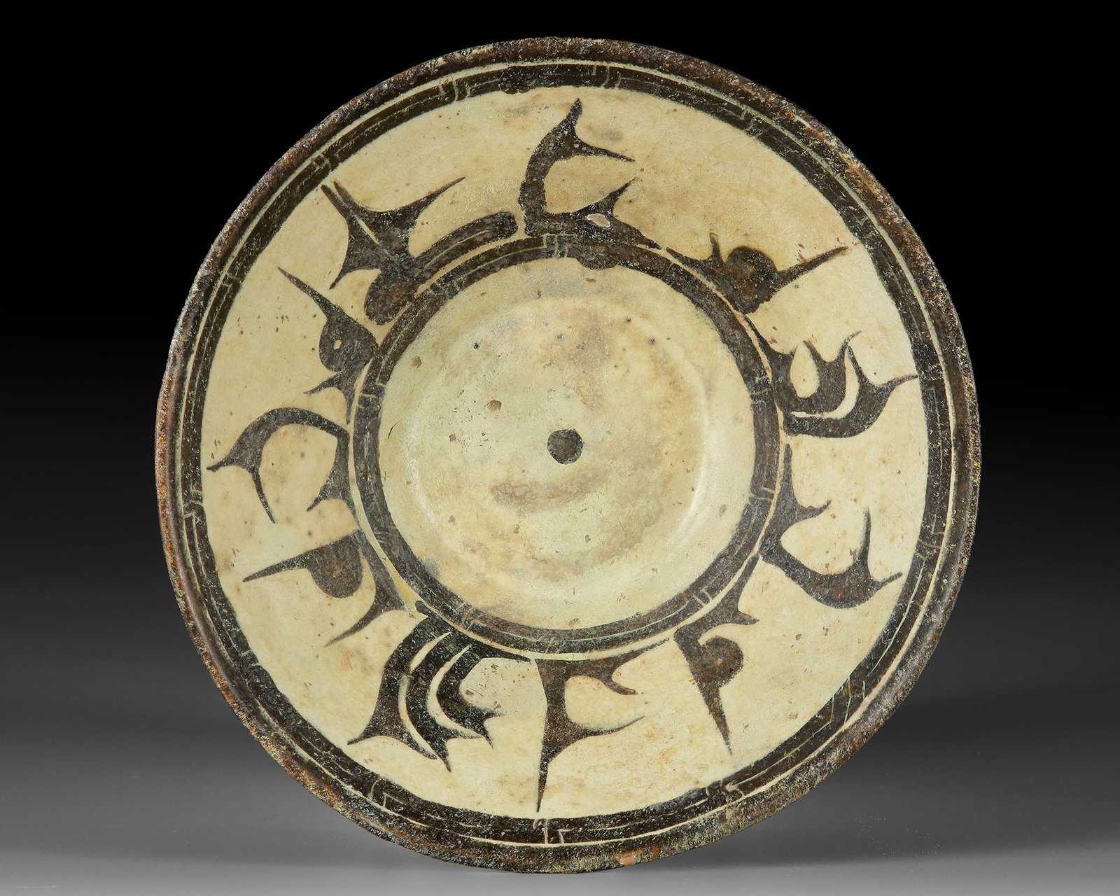 AN ISLAMIC NISHAPUR CALLIGRAPHIC POTTERY BOWL, EASTERN PERSIA, 10TH CENTURY: A Nishapur bowl painted in black/brown on a cream ground, with Kufic script as band, black/brown rim. Diameter: 23.5 cm. Height: 8 cm.