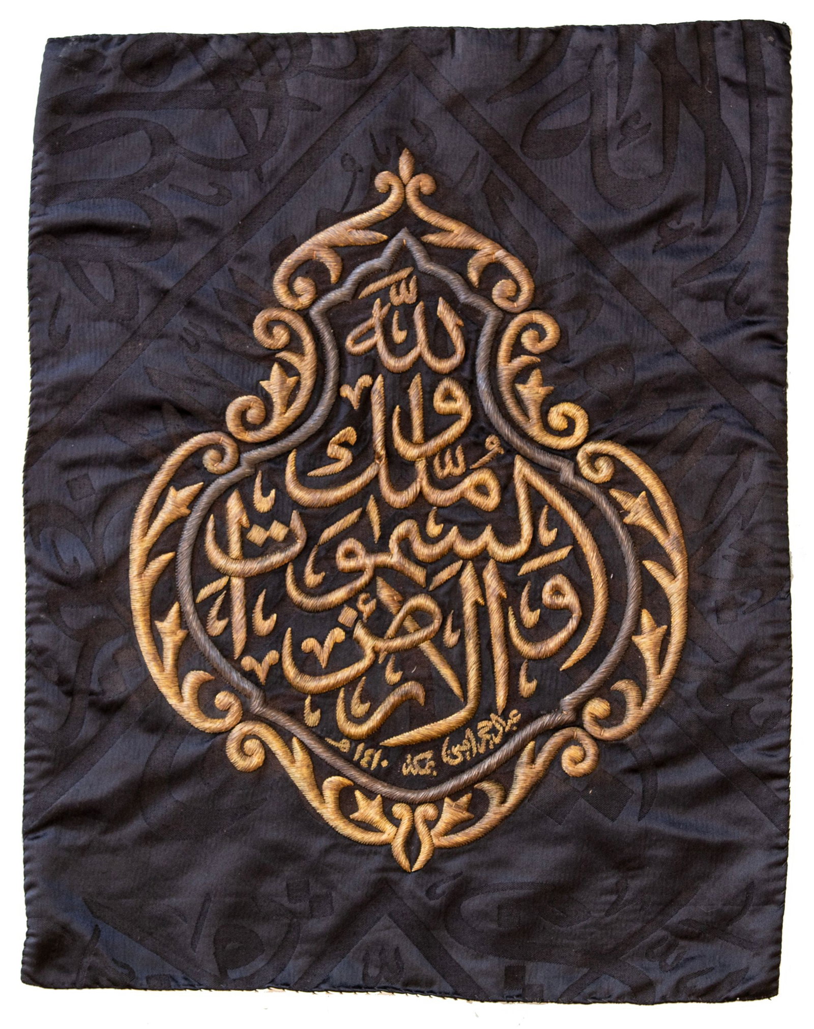 A GILT AND SILVER METAL-THREAD EMBROIDERED KISWAH FRAGMENT, MADE FOR THE HOLY KA'BA, SAUDIA ARABIA,: Of rectangular form, embroidered in gilt and silver metal thread on a black silk ground, this panel features a central cartouche inscribed in thuluth script, surrounded by intricate arabesque motifs. 