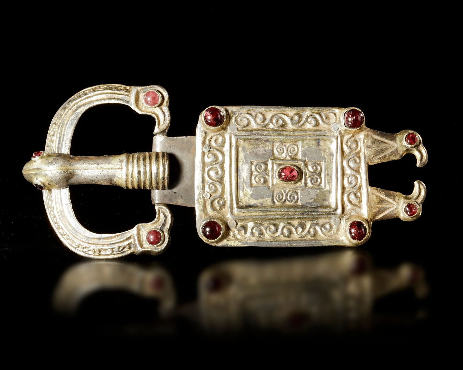 A MEROVINGIAN SILVER GILT SQUARE BELT BUCKLE WITH GARNETS, 6TH-7TH CENTURY AD,: A rectangular silver-gilt belt buckle with eagle heads and a snake head. And adorned with garnets. 15 by 7 cm. 119 gr.