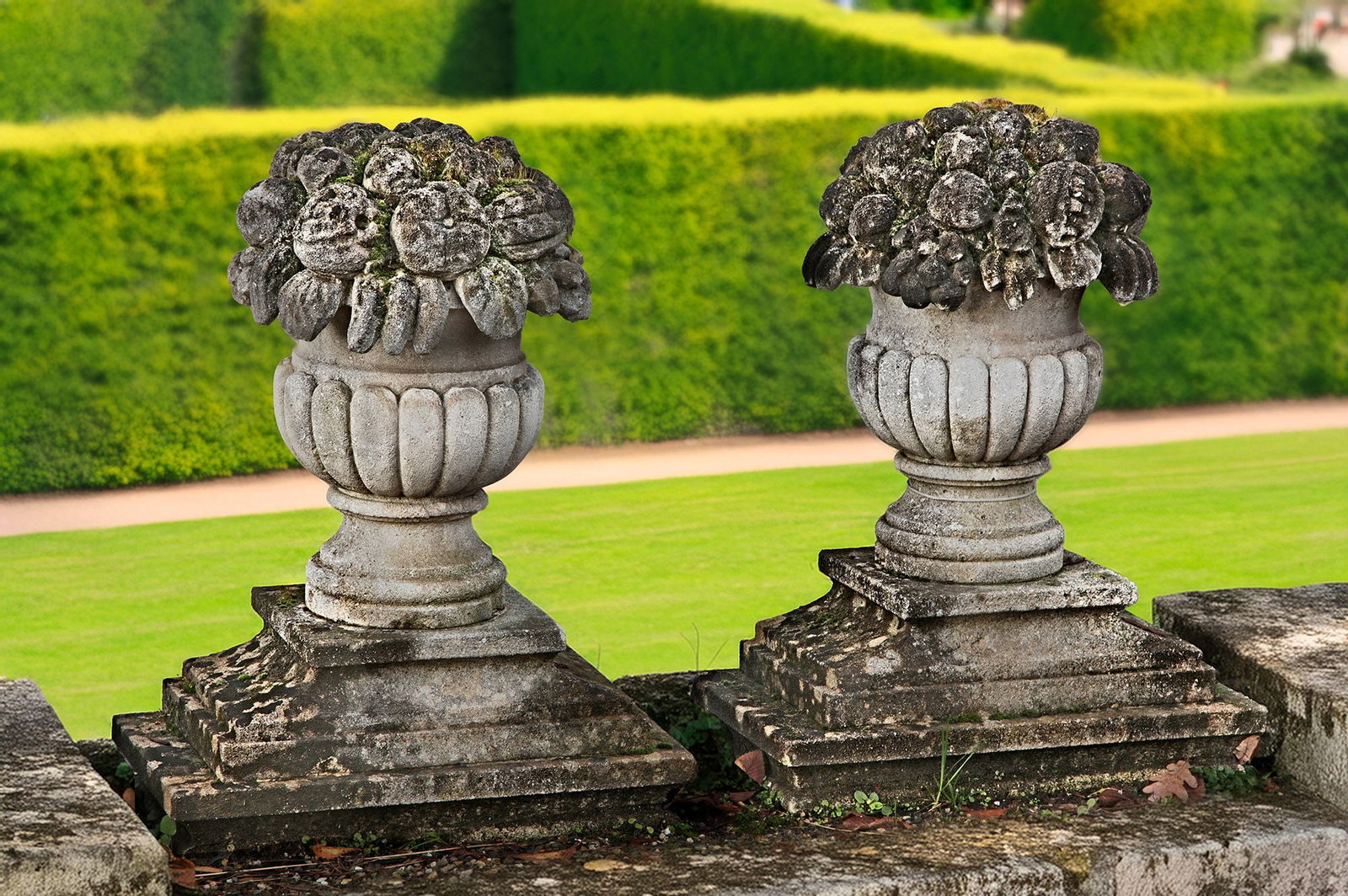 A PAIR OF CARVED LIMESTONE PIER FINIALS IN THE FORM OF FRUITING BASKETS, LATE 19TH OR EARLY 20TH: On stepped rectangular plinth bases. Height 62 cm. Width 49 cm. Depth 27 cm.