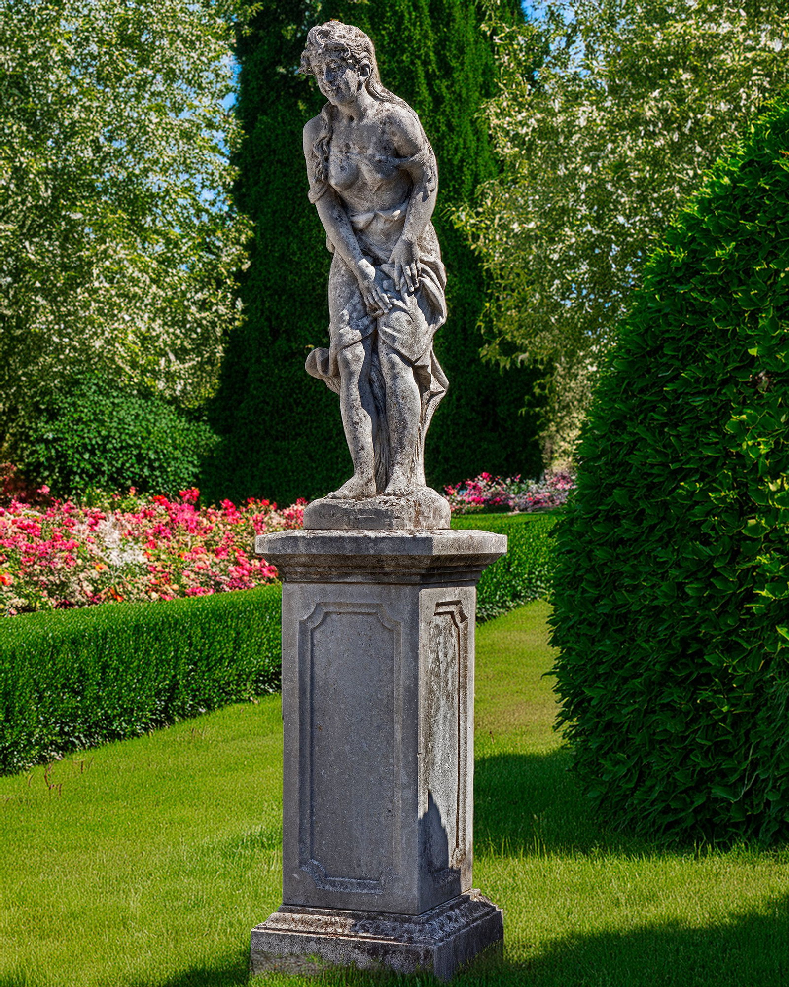A SCULPTED LIMESTONE MODEL OF A STANDING WOMAN, SECOND HALF 20TH CENTURY: Modelled standing but slightly hunched, her diaphanous robes covering her d?©colletage and with heavier drapes around her waist. Height 96 cm. Atop a square section panel sided pedestal, height 90 cm