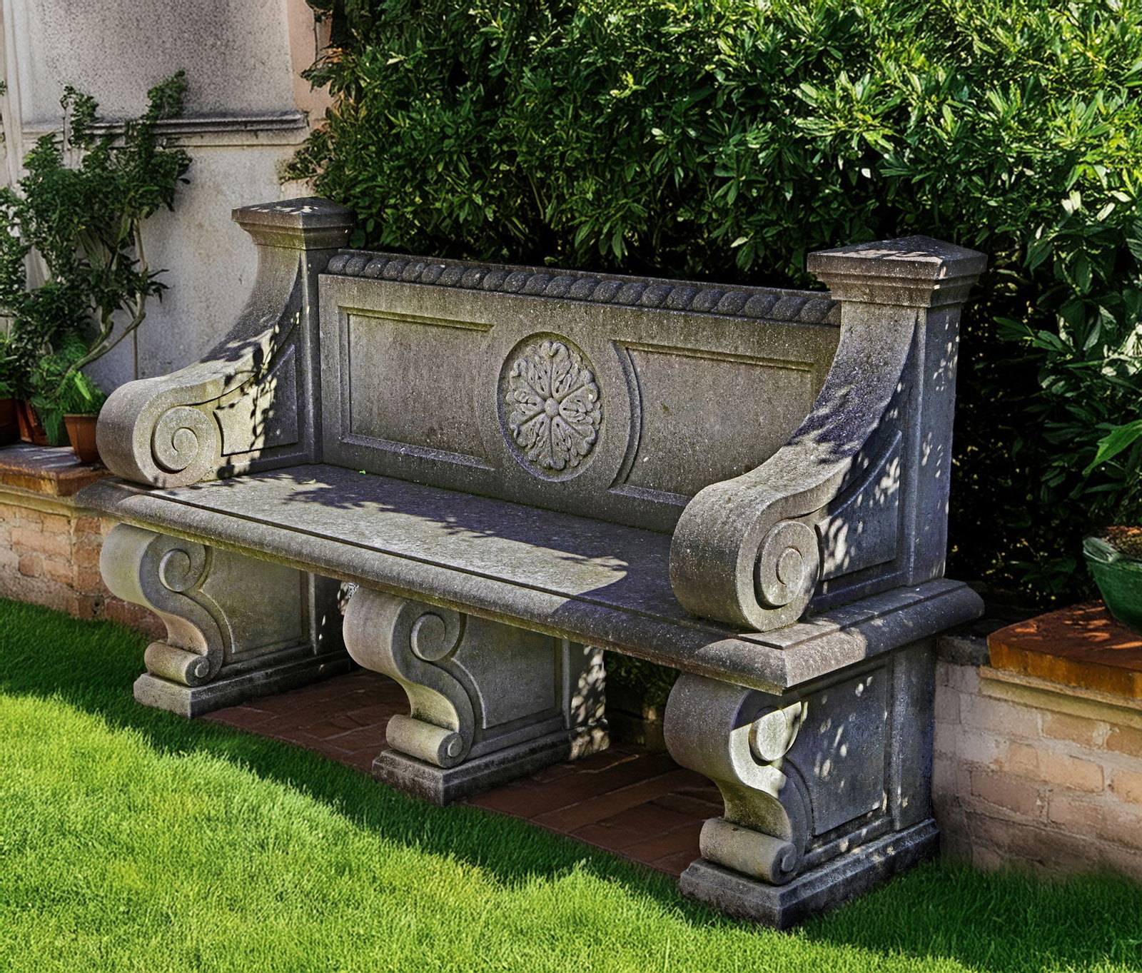 A CARVED LIMESTONE GARDEN SEAT IN LATE 18TH CENTURY FRENCH STYLE, LATE 20TH CENTURY: The rectangular backrest with ropetwist cresting rail above a panel back with central carved flowerhead, with volute shaped armrests to each side, the seat on three conforming supports. Height 103 cm.
