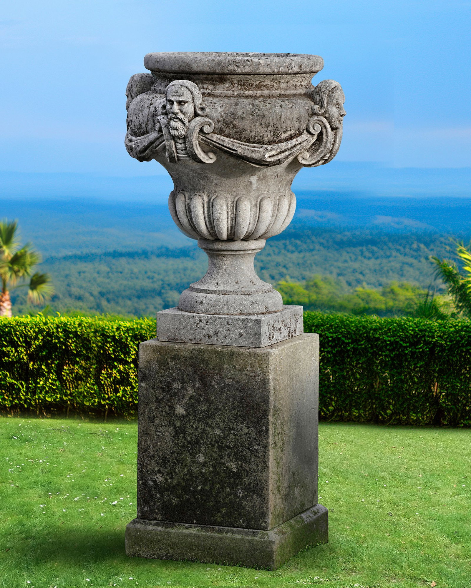A CARVED LIMESTONE PLANTER, SECOND HALF 20TH CENTURY: Of urn form, the body applied with scroll supported busts issuing swags, on a pedestal. Height overall 150 cm.