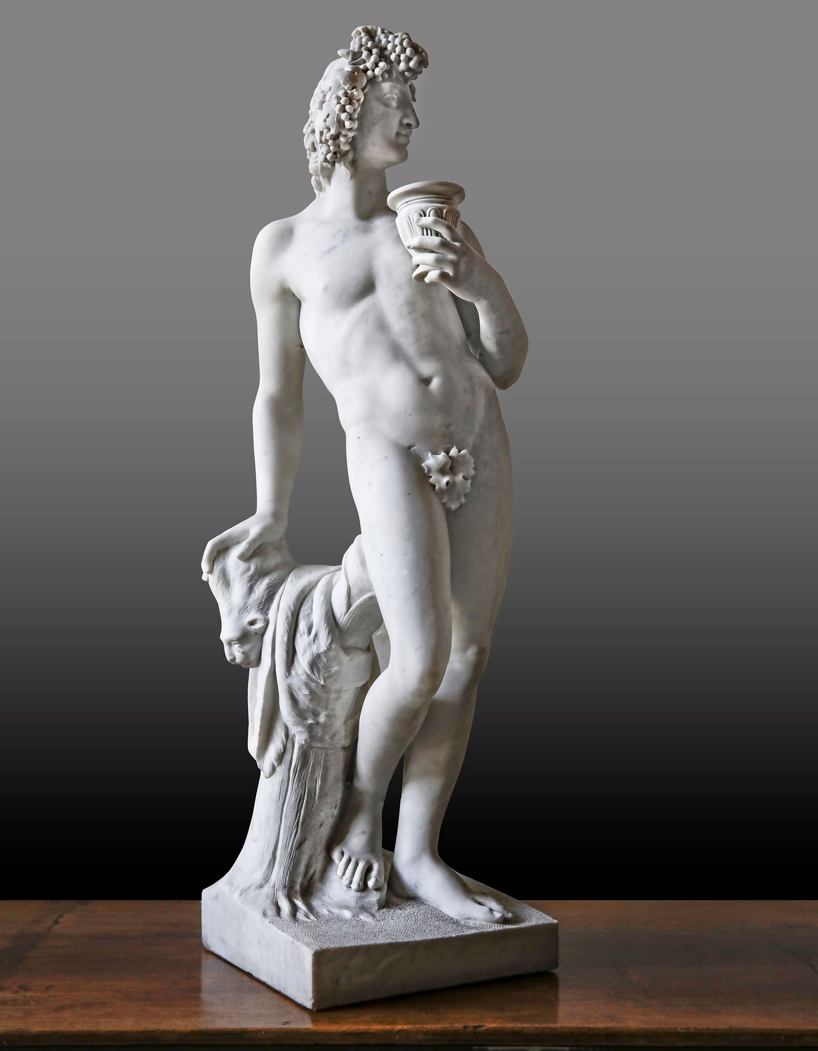 A SCULPTED MARBLE MODEL OF BACCHUS, LATE 20TH CENTURY: Portrayed nude but for a fig-leaf, and typically depicted holding his wine cup, nonchalantly resting on a support. Height 98 cm. Square at the base 28 cm.