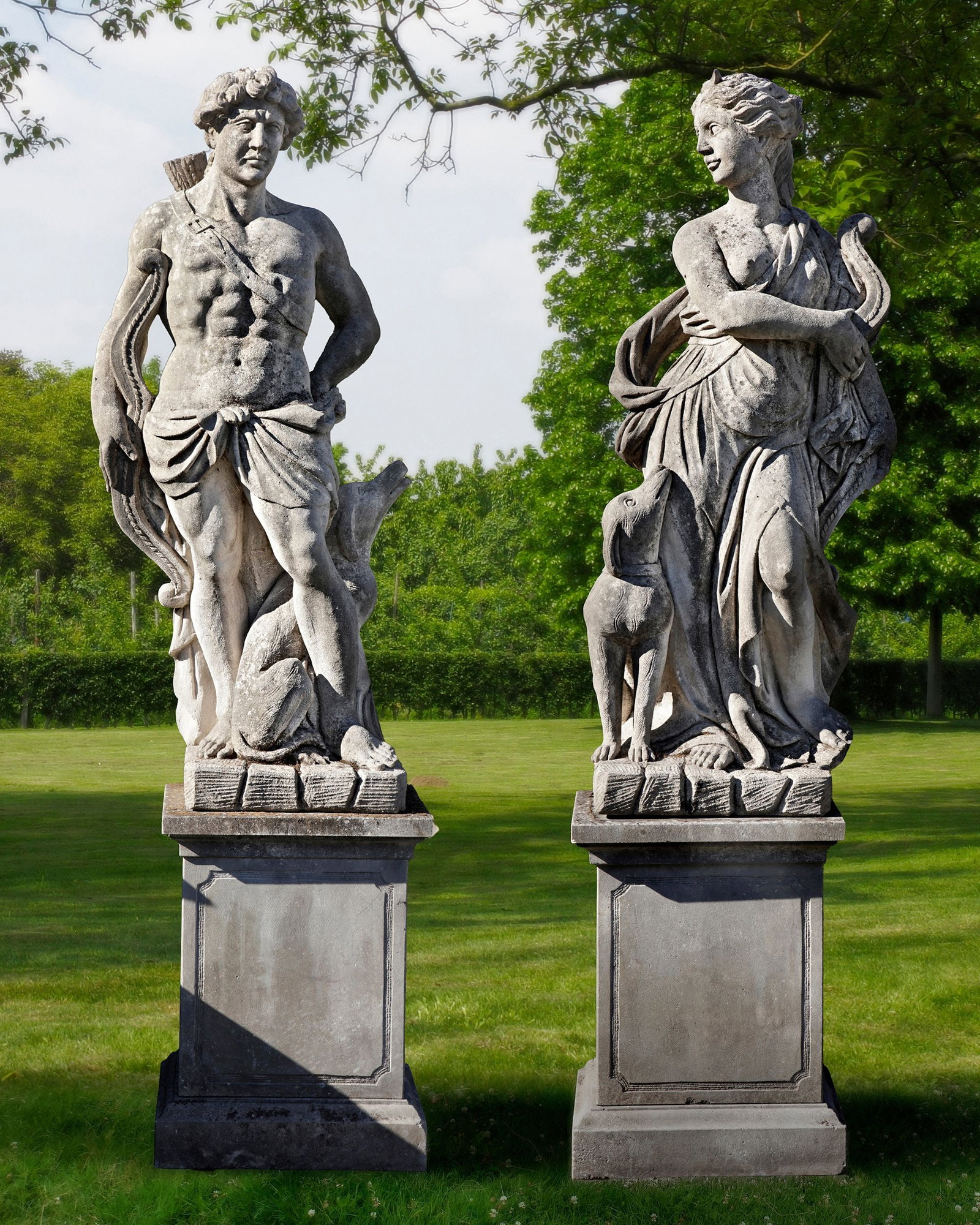 A PAIR OF SCULPTED LIMESTONE LIFESIZE FIGURES OF APOLLO AND DIANA, SECOND HALF 20TH CENTURY: Modelled opposing, nude and draped, with their hunting equipment, each with a hound to their side. Height each approximately 170 cm. Atop pedestals, height 80 cm., square 62 cm. Height overall 250 cm.