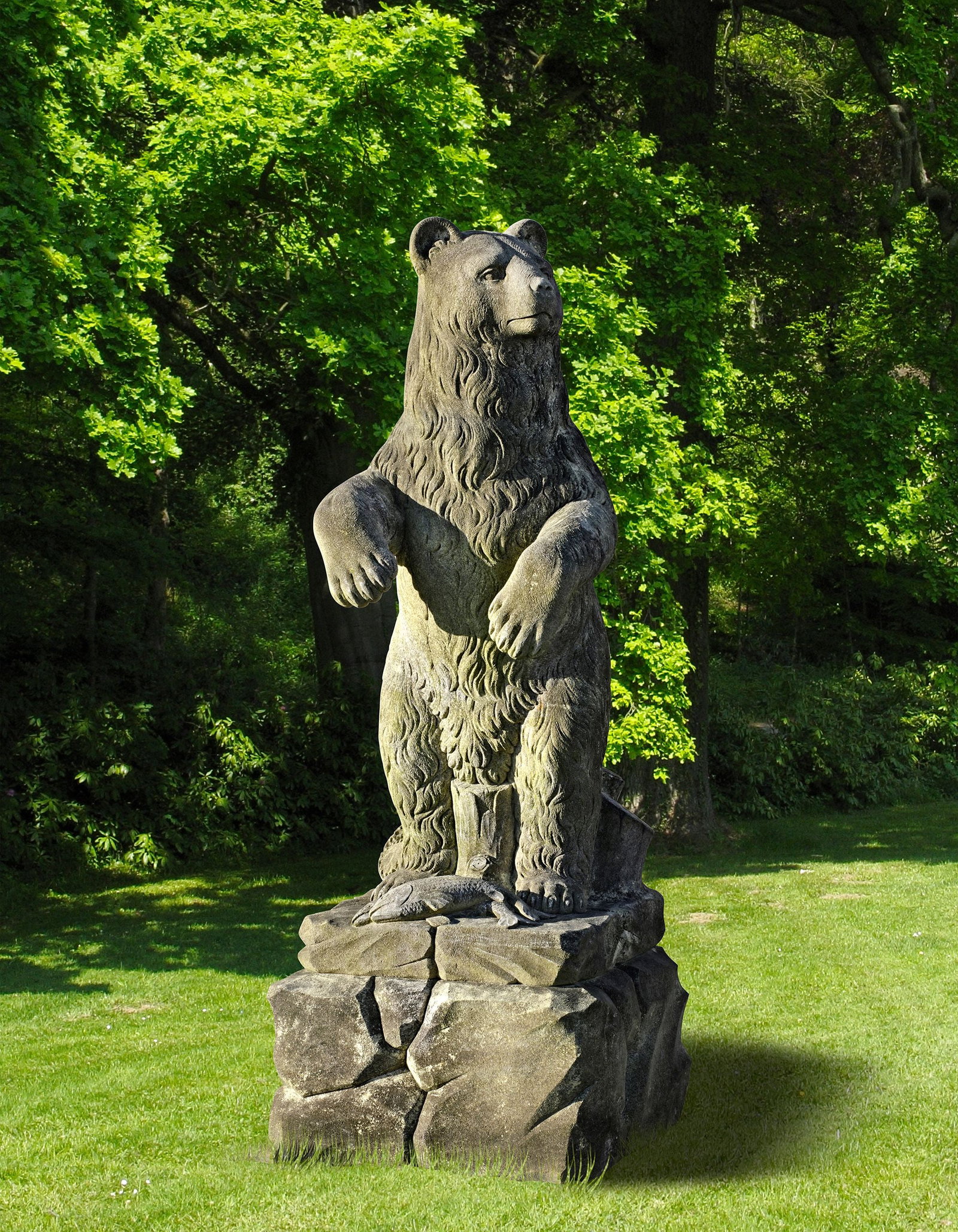 A SCULPTED LIMESTONE MODEL OF A GRIZZLY BEAR OF RECENT MANUFACTURE: The beast modelled standing with head turned and paws out in front, stood on an integral rockwork socle with two carved salmon to the front. Height 140 cm. Atop a rockwork plinth. Height 35 cm. Width 