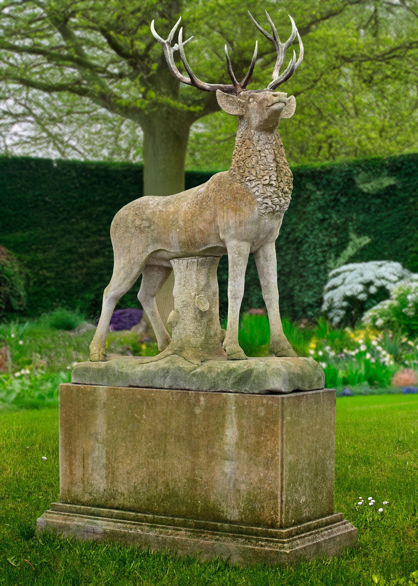 A LARGE AND IMPRESSIVE SCULPTED LIMESTONE AND ANTLER MOUNTED MODEL OF A STAG, LATE 20TH CENTURY: Naturalistically modelled standing and with naturalistic tree-trunk support and base. Height 250 cm. Width 165 cm. Depth 55 cm. Atop a rectangular section limestone pedestal, height 101 cm. width 196 