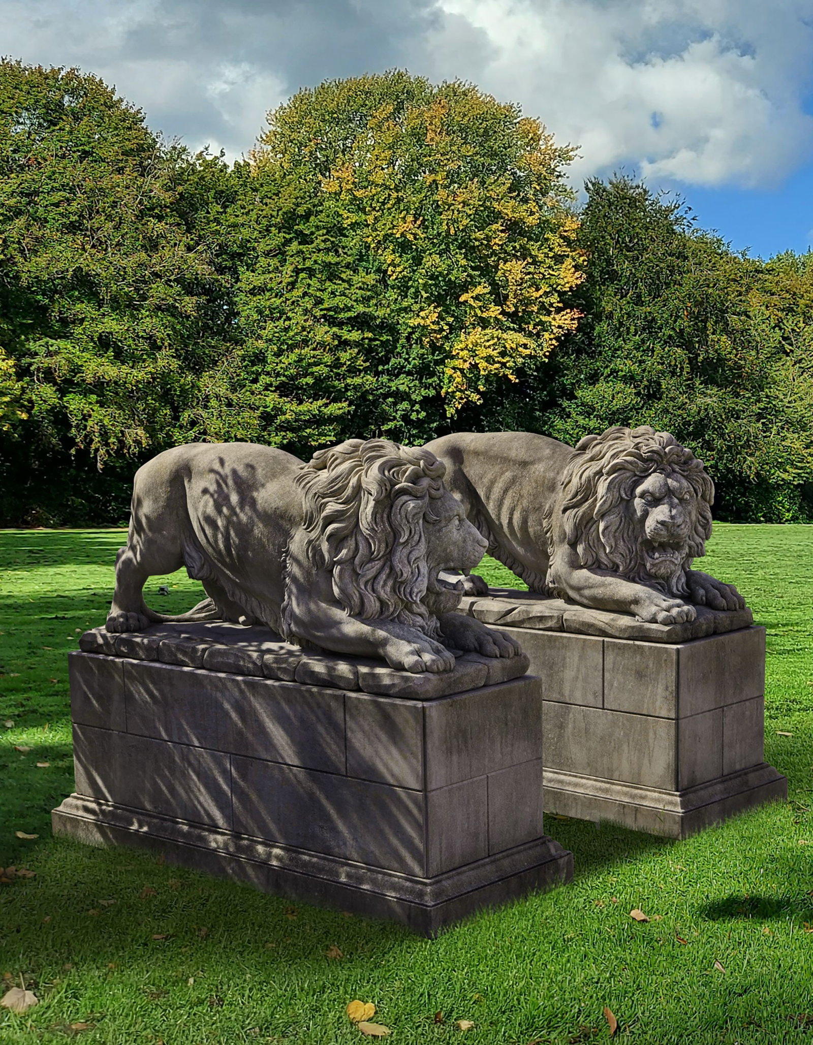 A PAIR OF SCULPTED LIMESTONE MODELS OF LIONS, SECOND HALF 20TH CENTURY: Each modelled above a naturalistic rockwork base. Height 69 cm. Length 158 cm. Width 51.5 cm. Atop simulated block-work pedestal bases, height 65.5 cm., length 177 cm,. width at the base 66.5 cm. Heig