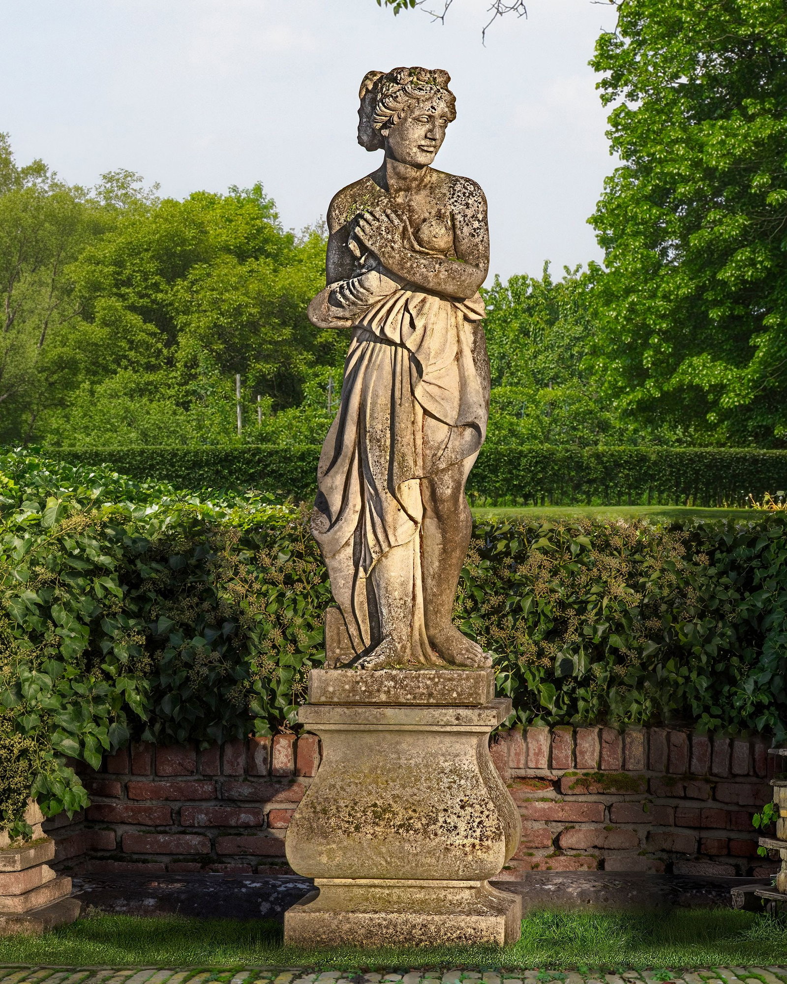 A SCULPTED LIMESTONE MODELS REPRESENTING VENUS, EACH FIRST QUARTER 20TH CENTURY: Portrayed standing and scantily draped, clutching right breast and robes to her midriff. Atop a square section baluster pedestal, height 59 cm. square 47 cm. Height overall approximately 209 cm.