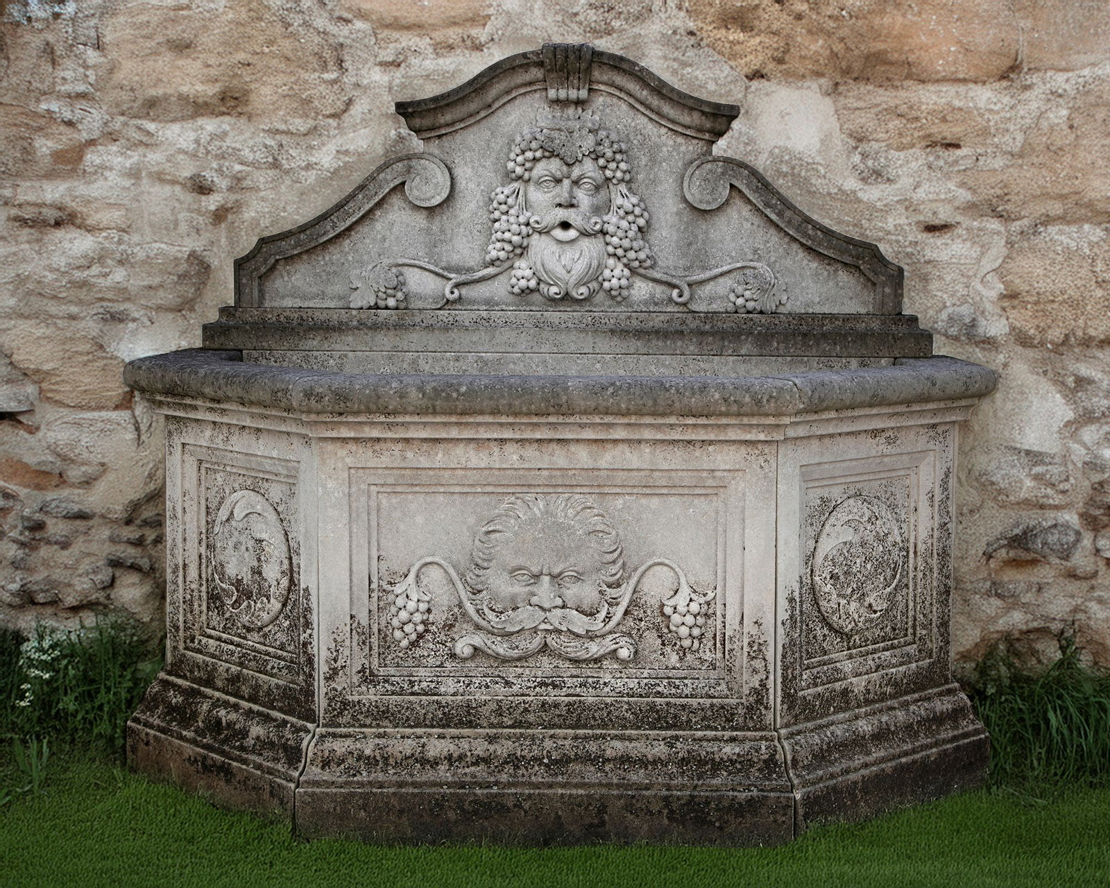 A CONTINENTAL SCULPTED LIMESTONE WALL FOUNTAIN, LATE 20TH CENTURY: The shaped backplate modelled as a pediment with Bacchic mask in relief, the deep basin with canted front corners, the front with a scallop-shell and foliate work in recessed relief, above a molded ba
