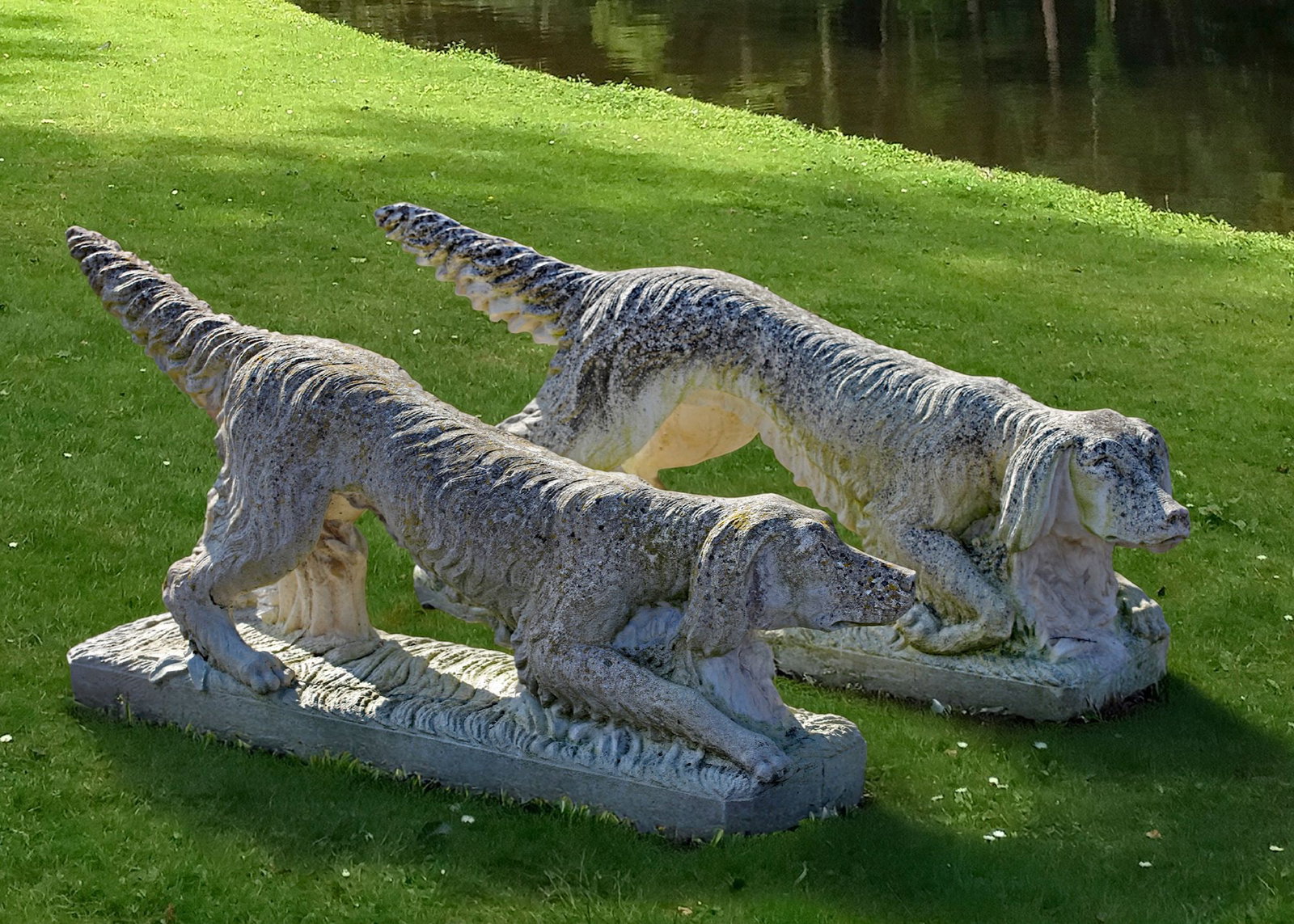 A PAIR OF COMPOSITION STONE HUNTING DOGS, 20TH CENTURY: Modelled opposing and each body lowered in pointing position and with one front paw outstretched the other raised. Height 65 cm. Length 145/155 cm. Width 35 cm.