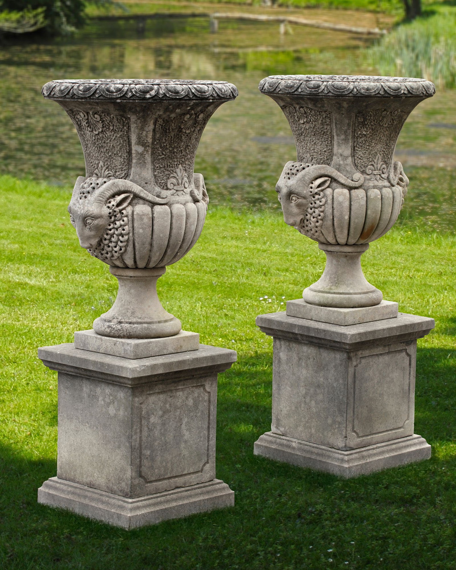 A PAIR OF CONTINENTAL SCULPTED VASES WITH RAMSHEAD: The design originates from the Neoclassical period (c. 1750â€“1820) and subsequently became very popular in 19th- and early 20th-century garden architecture. The ramâ€™s head on the si