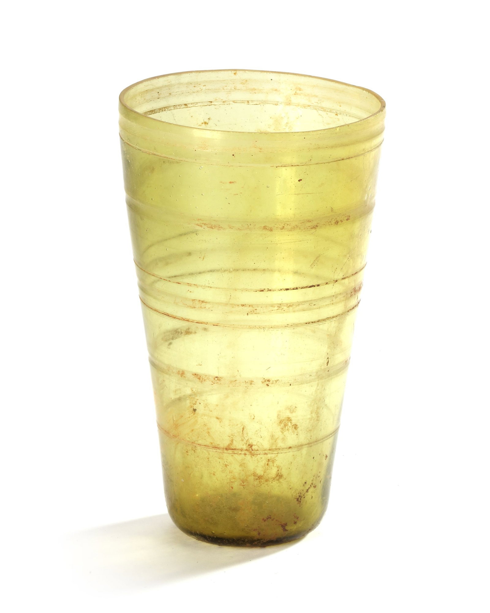 AN UMAYYAD GLASS BEAKER, NEAR EAST, 7TH-8TH CENTURY: Of tapering cylindrical form broadening toward the mouth, clear glass body with rings around it. 14.7 by 8.5 cm.
