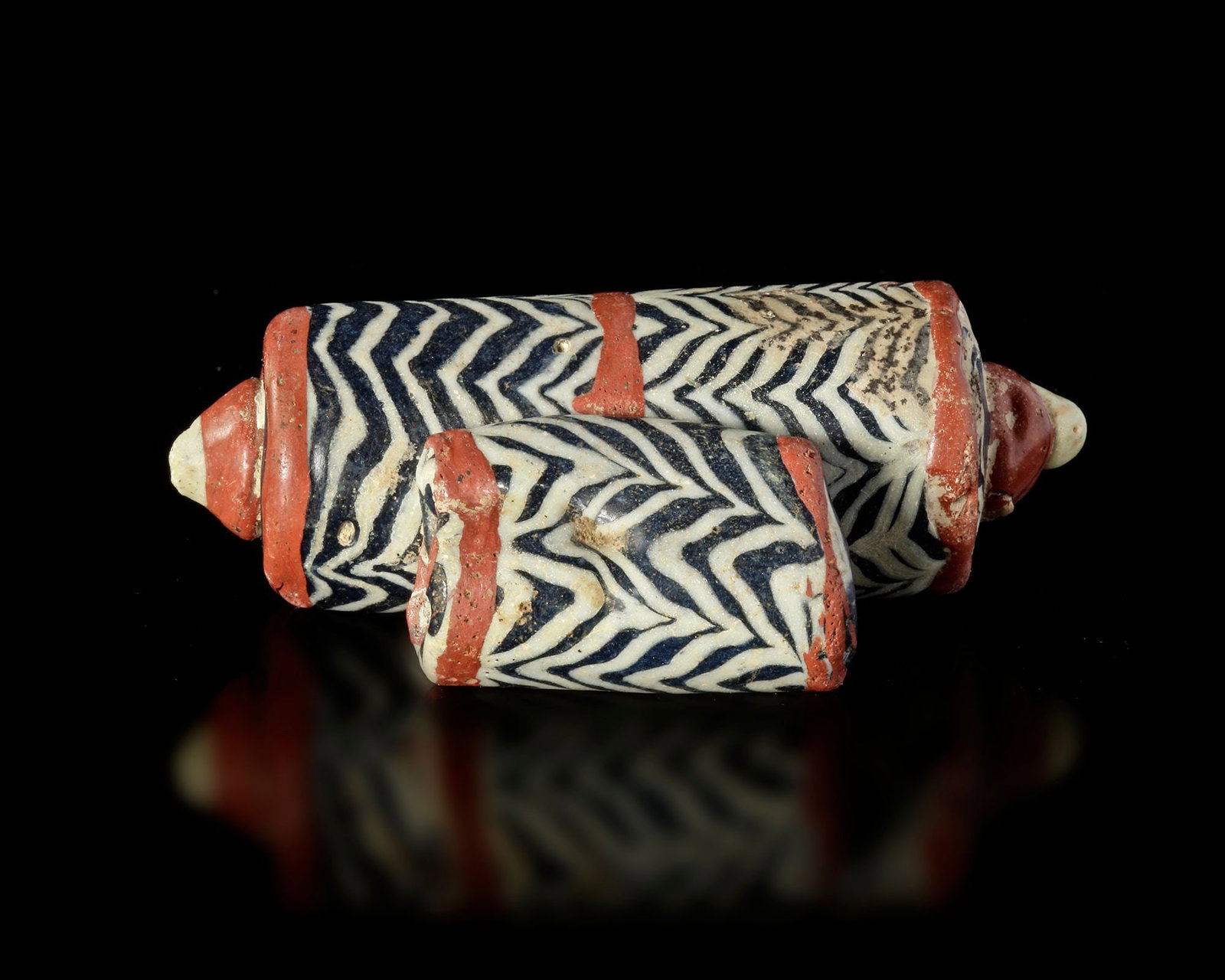 AN EARLY ISLAMIC GLASS BEAD, SYRIA, 900â€“1200 AD: A rare cylindrical glass bead from the early Islamic period, decorated with striking black and white chevron patterns and red bands. Such beads were produced in the Levant and traded widely across the