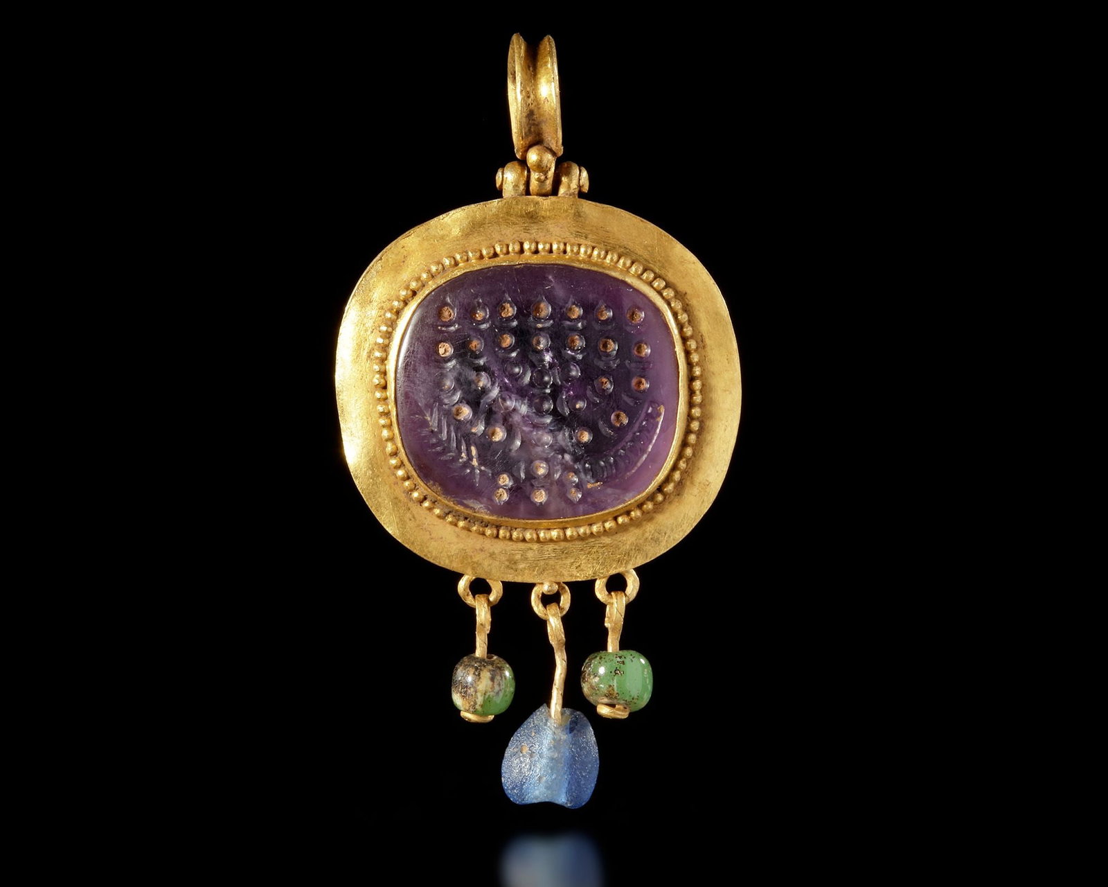 A LATE ROMANâ€“BYZANTINE GOLD PENDANT WITH AMETHYST MENORAH INTAGLIO, 5TH-7TH CENTURY AD: Gold pendant set with a deep purple amethyst intaglio engraved with a seven-branched menorah. To the left appears a shofar, and to the right an ear of wheat, forming a trio of important Jewish ritual 