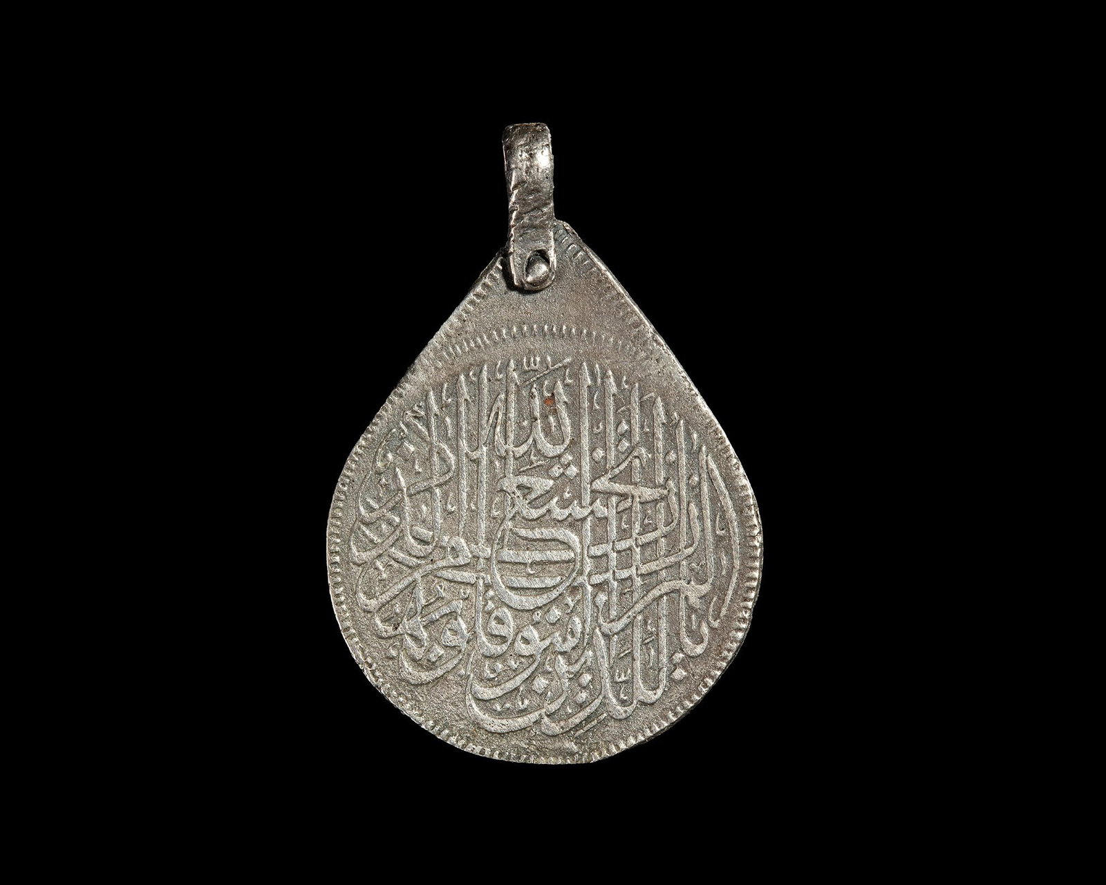 AN OTTOMAN SILVER QURANIC AMULET PENDANT, 19TH CENTURY: An Ottoman silver pendant of teardrop form, finely inscribed on both sides with Quranic verses and devotional Arabic calligraphy. Possibly worn as a protective amulet. 9 gr. 40 by 27 mm.