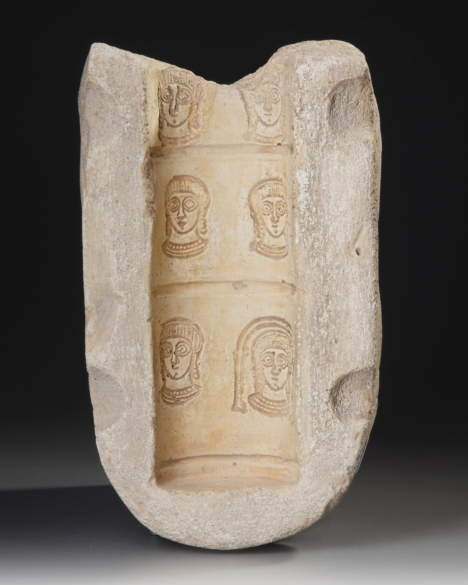 A ROMAN PLASTER MOULD FOR A CYLINDRICAL RED WARE VESSEL, 4TH-5TH CENTURY AD: This plaster mould is half of an ensemble which would have served to make cylindrical red ware vases from the workshops of central Roman north Africa. The type shows the facing bust of a woman who mig
