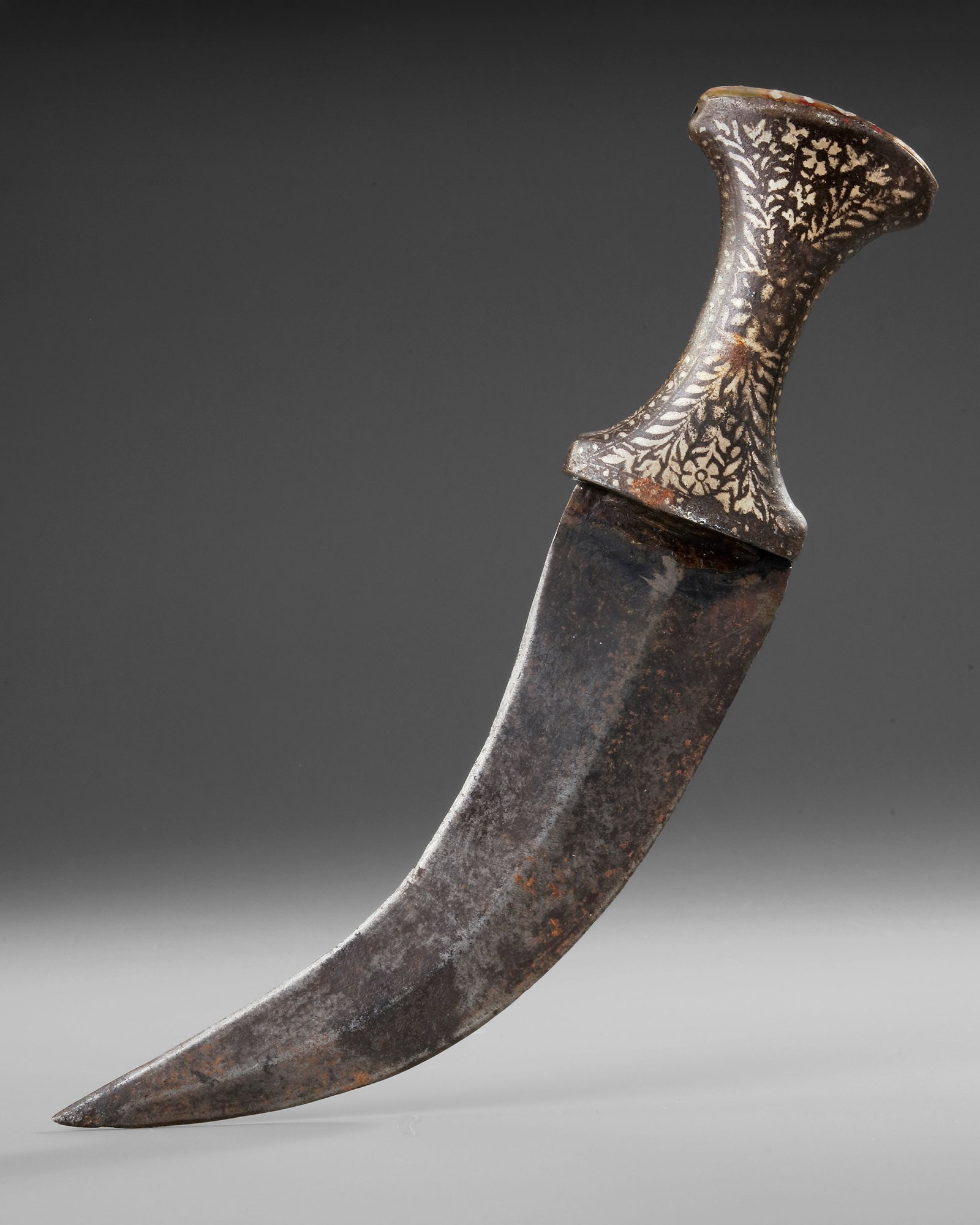 AN INDIAN SILVER-INLAID KUFTGARI DAGGER, 18TH CENTURY: An Indian kuftgari dagger featuring a hand-forged curved steel blade and a beautifully decorated hilt adorned with intricate silver floral inlay in the classic kuftgari technique. The ergonomic pistol