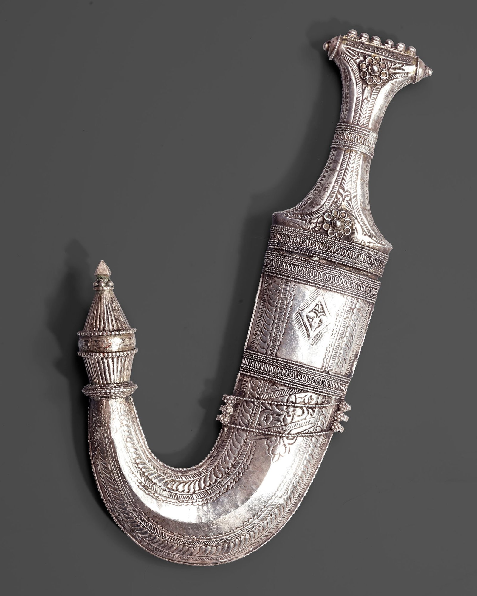A SILVER YEMENI DAGGER (JANBIYA), EARLY 20TH CENTURY: A finely crafted Yemeni janbiya with a deeply curved form and an elaborately worked silver scabbard. The surface is decorated with engraved and chased geometric and floral motifs L. 29,5 cm. 392 gr.