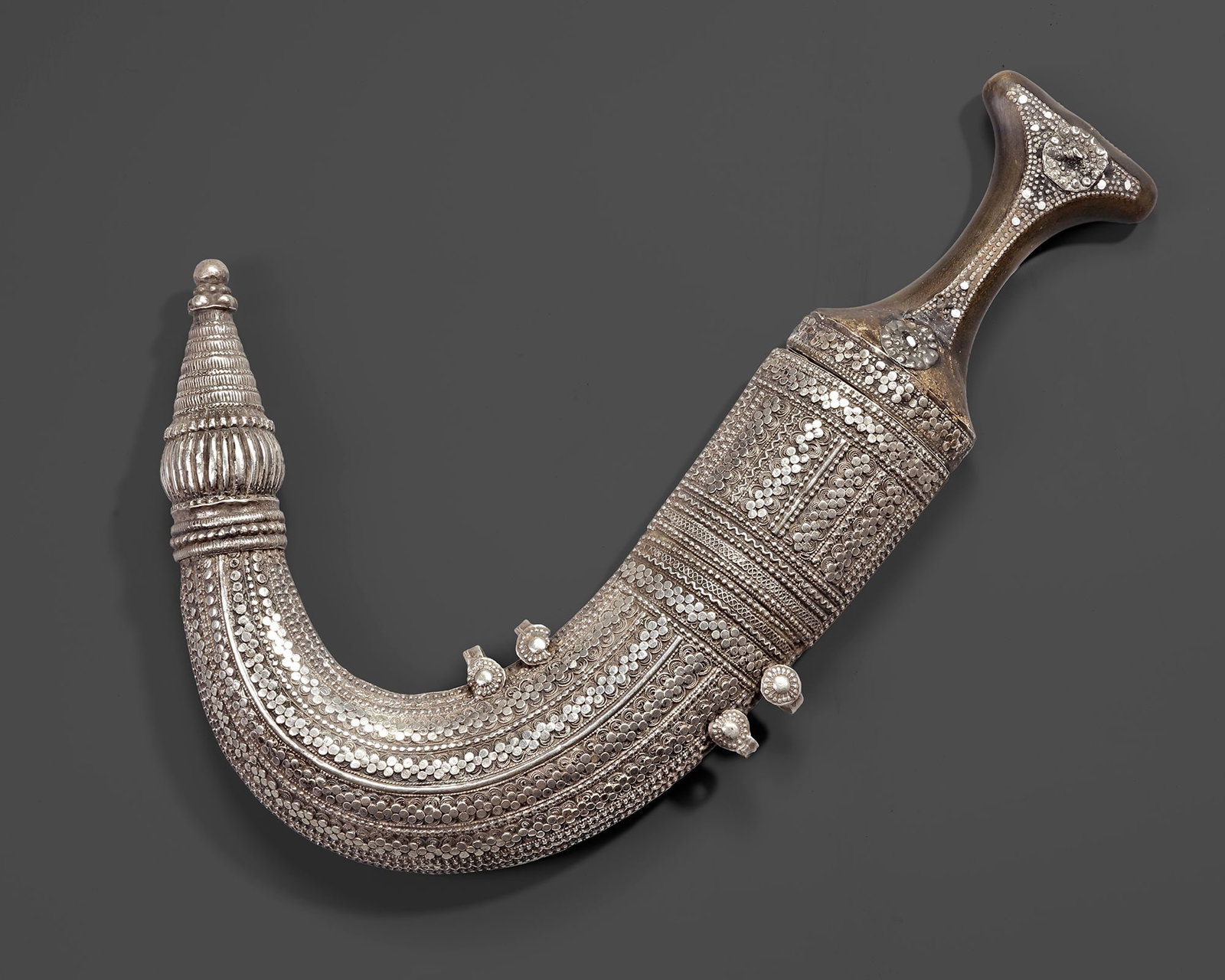 A SILVER YEMENI DAGGER (JANBIYA), EARLY 20TH CENTURY: A finely crafted Yemeni janbiya with a deeply curved scabbard richly decorated in intricate silver filigree and dotted repouss?© work. The elegant hilt, traditionally shaped and adorned with detailed
