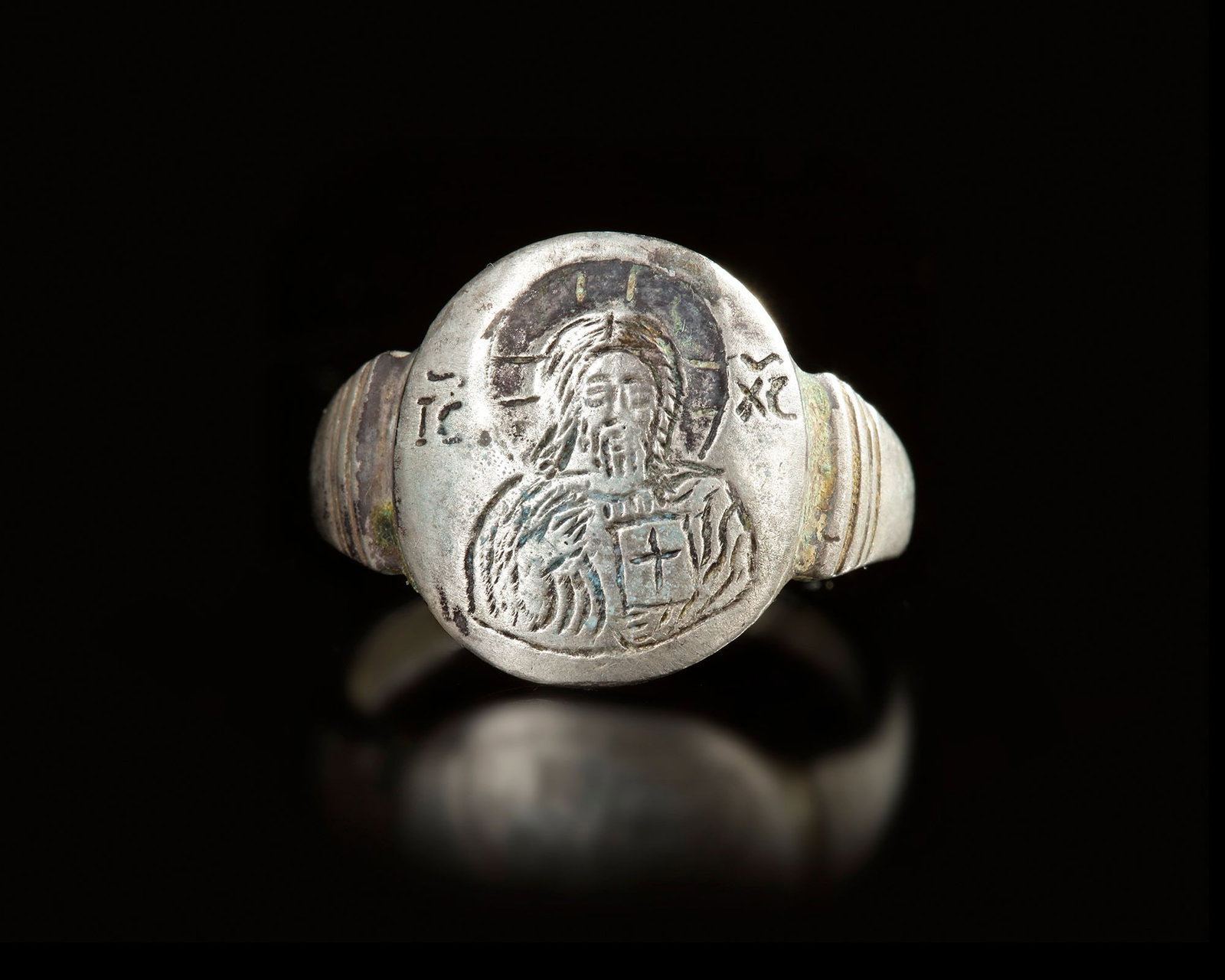 A BYZANTINE SILVER RING DEPICTING A SACRED FIGURE: A Byzantine silver ring with an engraved oval bezel depicting a haloed sacred figure holding a cross, surrounded by decorative symbols. EU size 52, US size 6