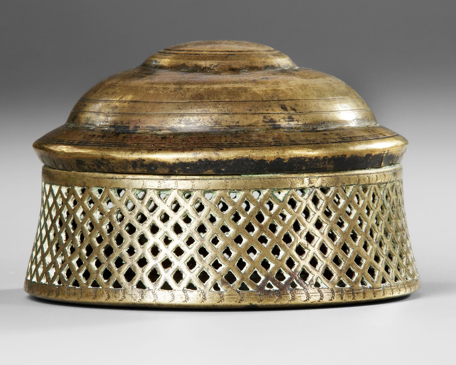 AN INCENSE BURNER YEMEN, 17TH CENTURY: Brass incense burner of domed form, featuring a beautifully pierced lattice body designed to diffuse aromatic smoke. The stepped lid and circular base are accentuated with concentric ring decoration, 