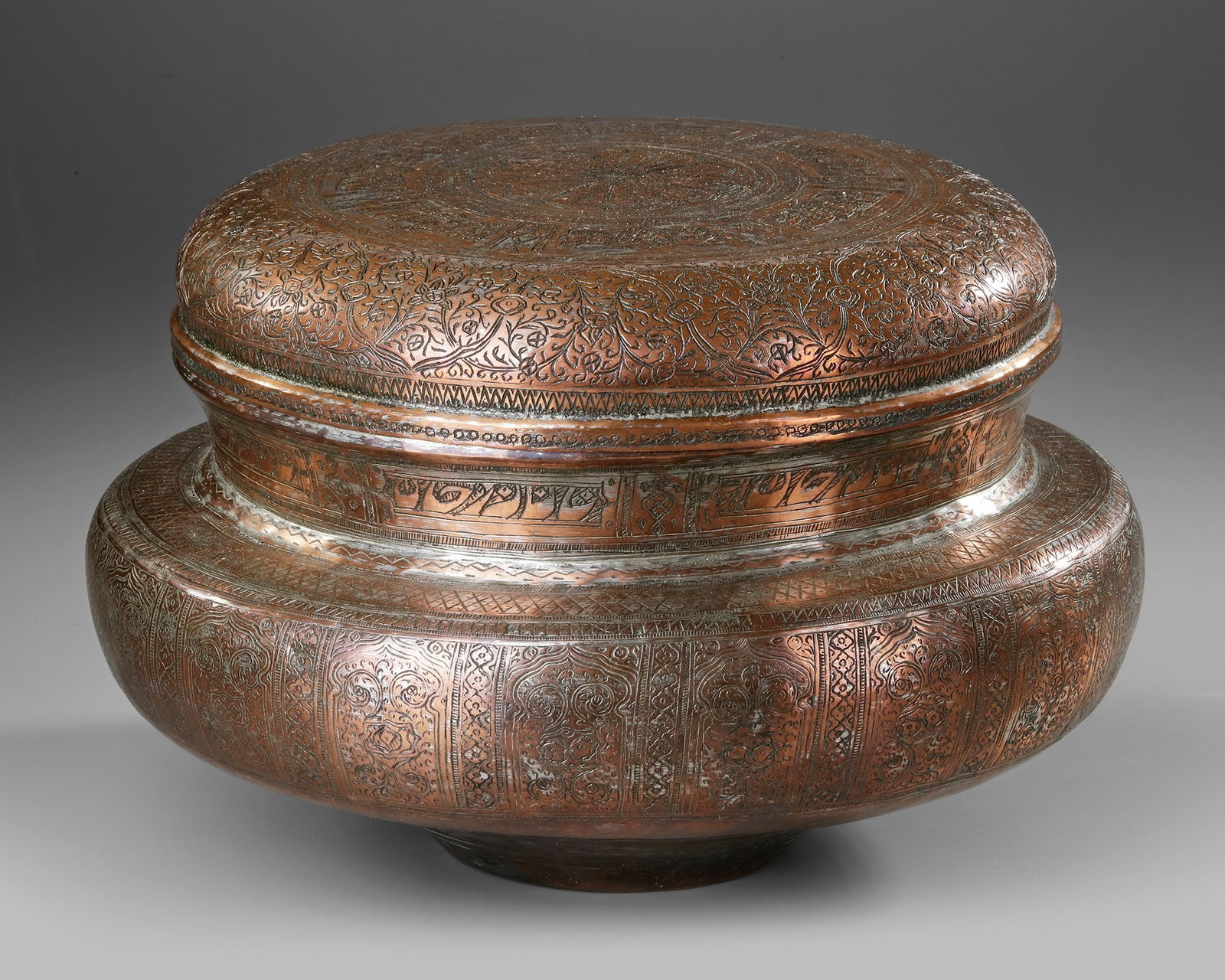 ENGRAVED POT WITH COVER, QAJAR PERSIA, 19TH CENTURY: A finely crafted Qajar-period metal pot with a fitted cover, richly decorated with intricate engraved floral patterns and elegant bands of Persian calligraphy. The domed lid features a central rosette