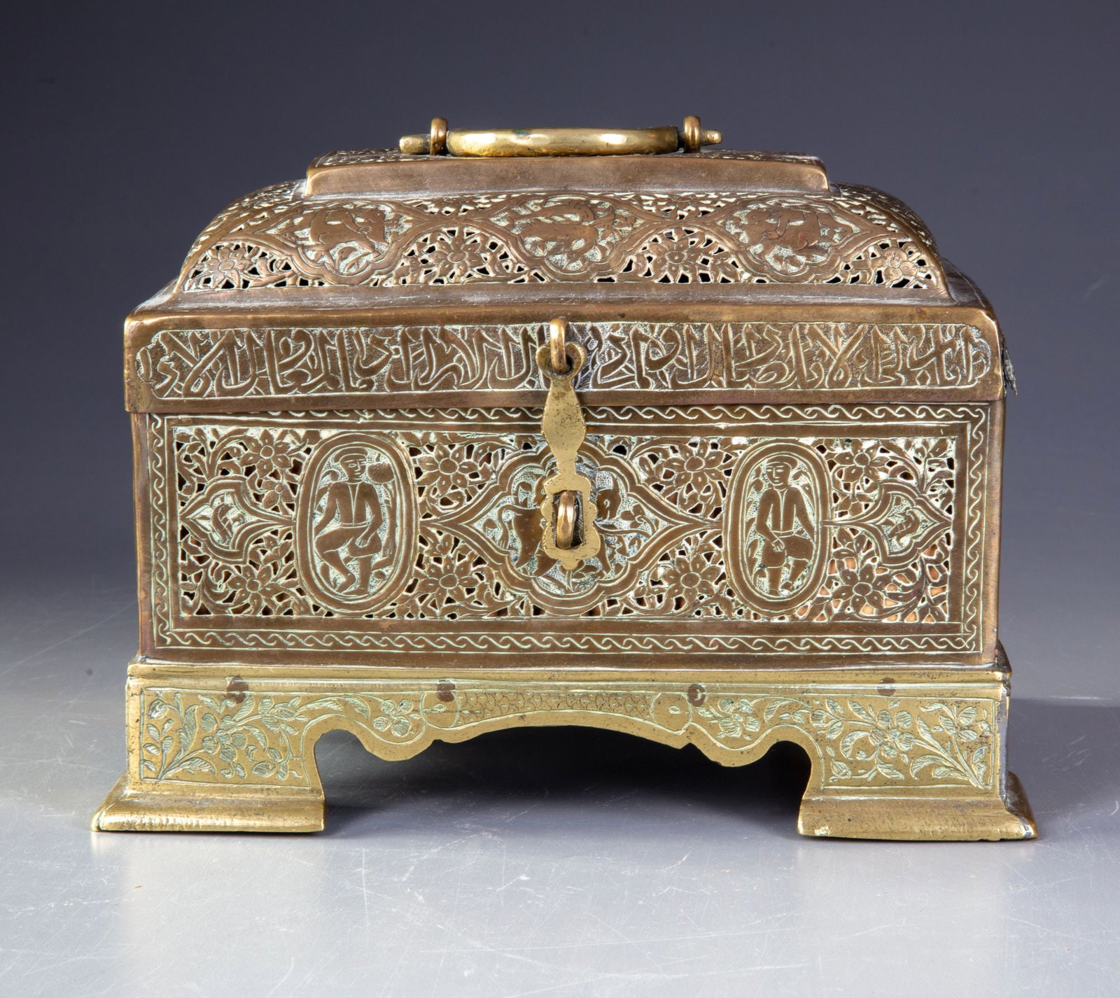 A QAJAR BRASS OPENWORK CASKET, PERSIA, 19TH CENTURY: Of rectangular form with domed hinged cover and carrying handle. The surfaces are richly decorated with intricate pierced arabesque and floral scrollwork, interspersed with engraved cartouches enclosi