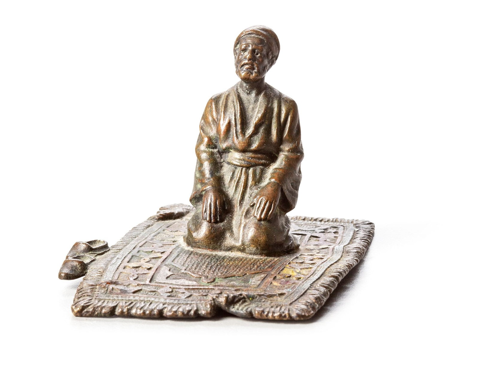A SMALL AUSTRIAN BRONZE FIGURINE, 19TH CENTURY: Austrian bronze figurine depicting a kneeling man in traditional attire upon a finely detailed prayer rug. Richly cast with expressive features and warm patina. 8 by 6 by 6 cm. 142 gr.