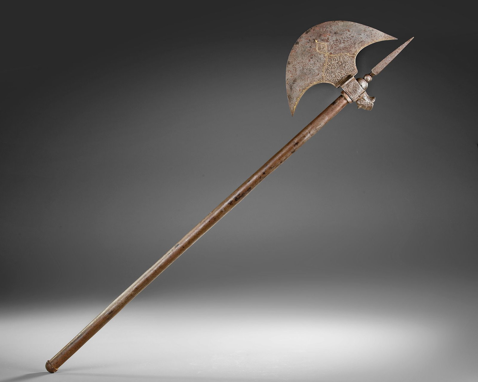 A QAJAR ENGRAVED AXE, PERSIA, 19TH CENTURY: A Persian Qajar axe featuring a broad crescent-shaped blade finely engraved with floral and calligraphic motifs. Mounted on a long wooden shaft, the head is complemented by a rear spike and decorative