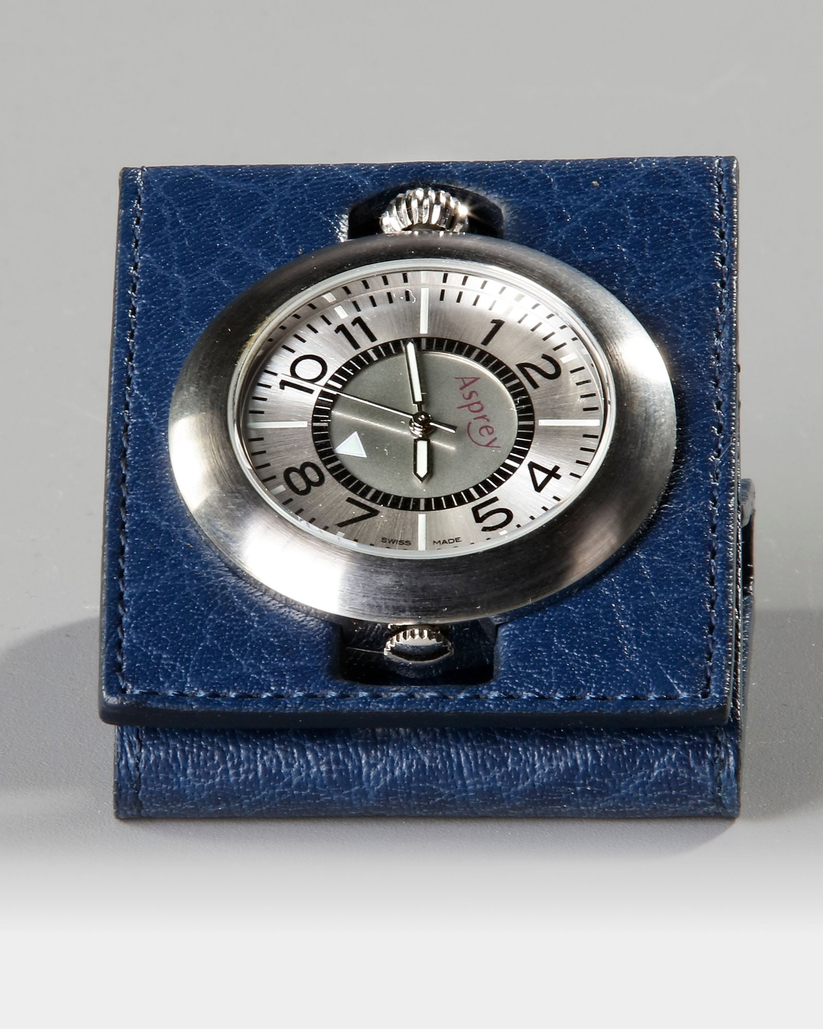 AN ASPREY TRAVEL CLOCK: A stylish Asprey Swiss-made travel clock, featuring a brushed metal case housed within an elegant blue leather folding cover. Combining refined design with practical portability, this compact timepiec