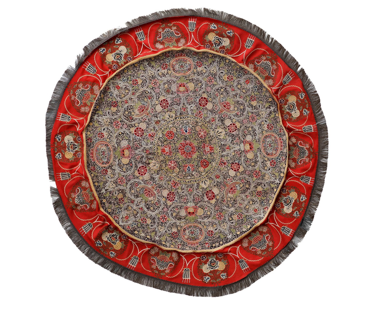 A RESHT EMBROIDERY CIRCULAR TABLE COVER, PERSIA, 19TH CENTURY: A finely embroidered circular textile featuring an intricate floral medallion within a dense scrolling vine field, framed by a vibrant red border of stylized floral motifs and finished with a soft fri