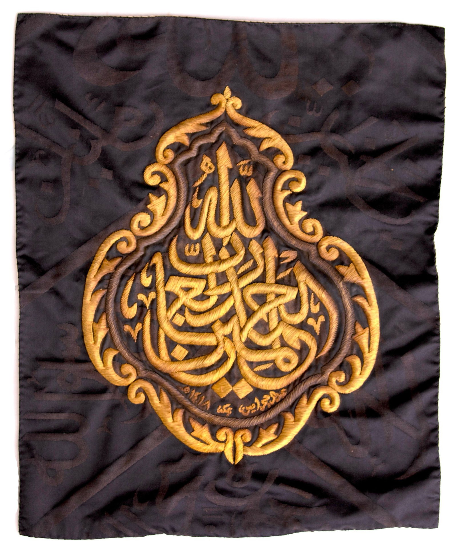A GILT AND SILVER METAL-THREAD EMBROIDERED KISWAH FRAGMENT, MADE FOR THE HOLY KAABA, SAUDI ARABIA,: Of rectangular form, embroidered in gilt a d silver metal thread on a black silk ground, this panel features a central cartouche inscribed in thuluth script, surrounded by intricate arabesque motifs. 