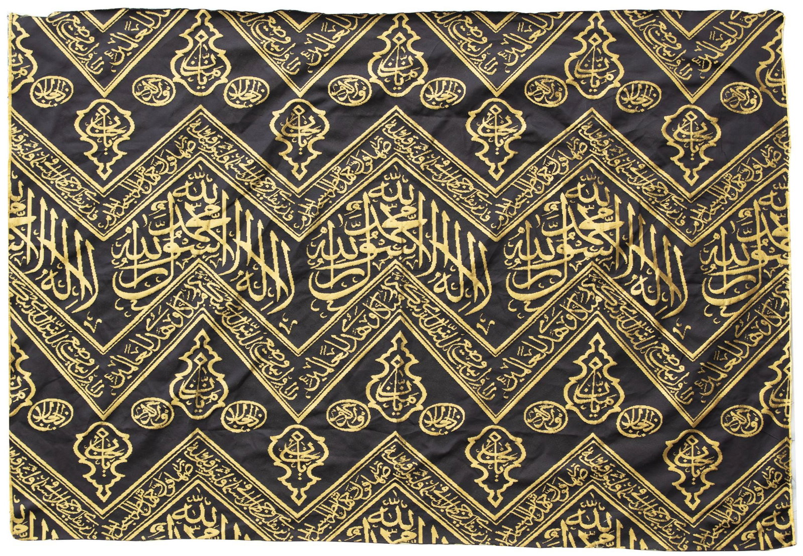 AN OTTOMAN CALLIGRAPHIC KISWA TEXTILE FRAGMENT, TURKEY OR EGYPT, 20TH CENTURY: A fragment from the inner curtain of the sacred kiswa that lines the interior wall of the Kaaba, woven in gilt-colored silk against a deep black ground. The design features chevron patterns incorporat