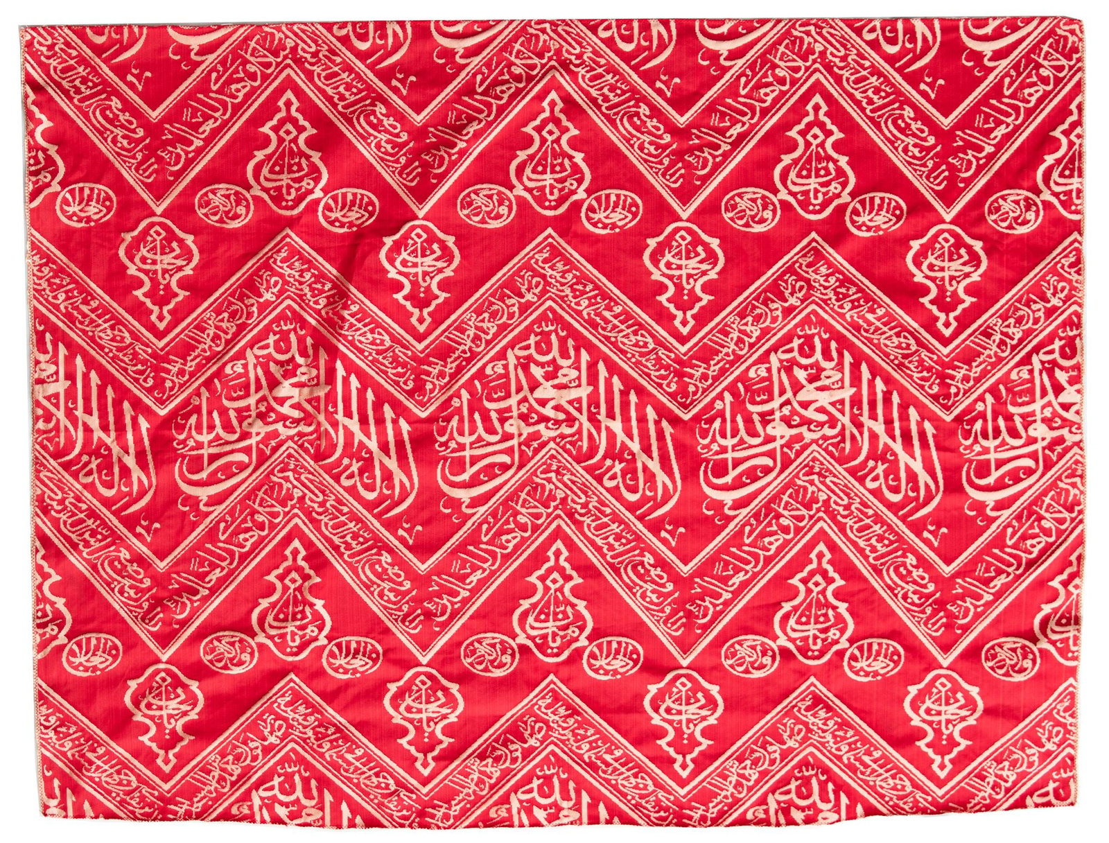 AN OTTOMAN RED EMBROIDERED SILK KISWA FRAGMENT, TURKEY OR EGYPT 20TH CENTURY: A fragment from the inner curtain of the sacred kiswa that lines the interior wall of the Kaaba, woven in cream-colored silk against a rich dark red background. The design features chevron patterns in