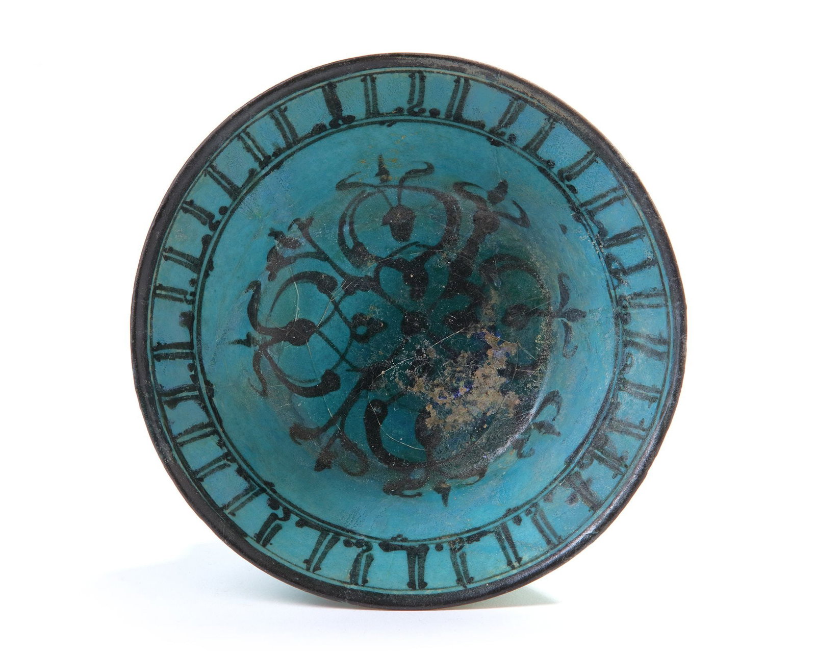 A RAQQA TURQUOISE GLAZED POTTERY BOWL, SYRIA, 13TH-14TH CENTURY: Rising from short vertical foot to a slightly everted rim, the interior painted in black under the turquoise glaze with a central roundel of interlocking flower sprays, to the rim with a band of Arabi