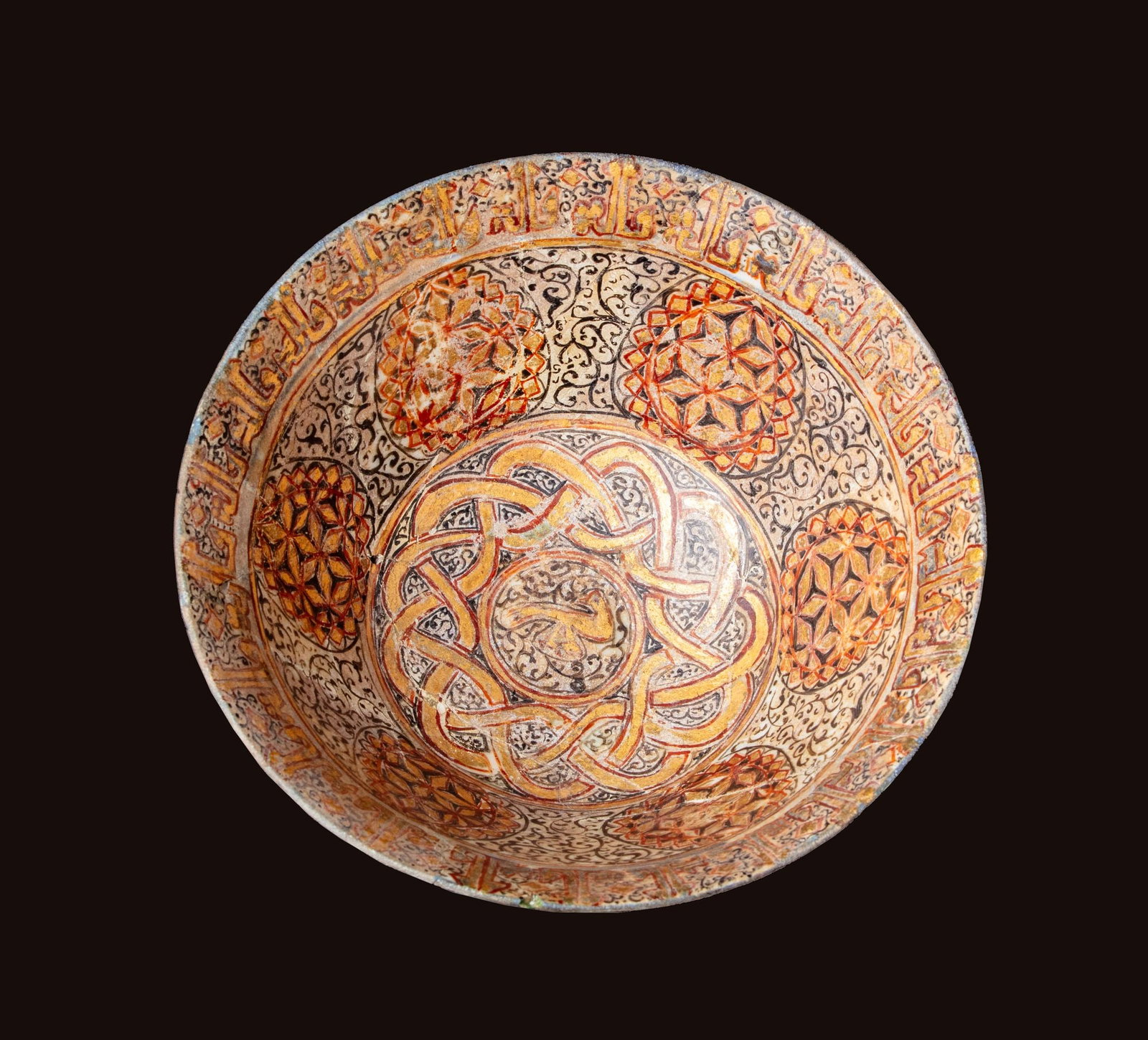 A KASHAN LUSTRE-PAINTED BOWL, PERSIA, 12THâ€“13TH CENTURY: This finely crafted Kashan bowl exemplifies the sophisticated lustreware tradition of medieval Iran. Its interior is richly decorated with interlaced arabesques, geometric star motifs, and a band of K