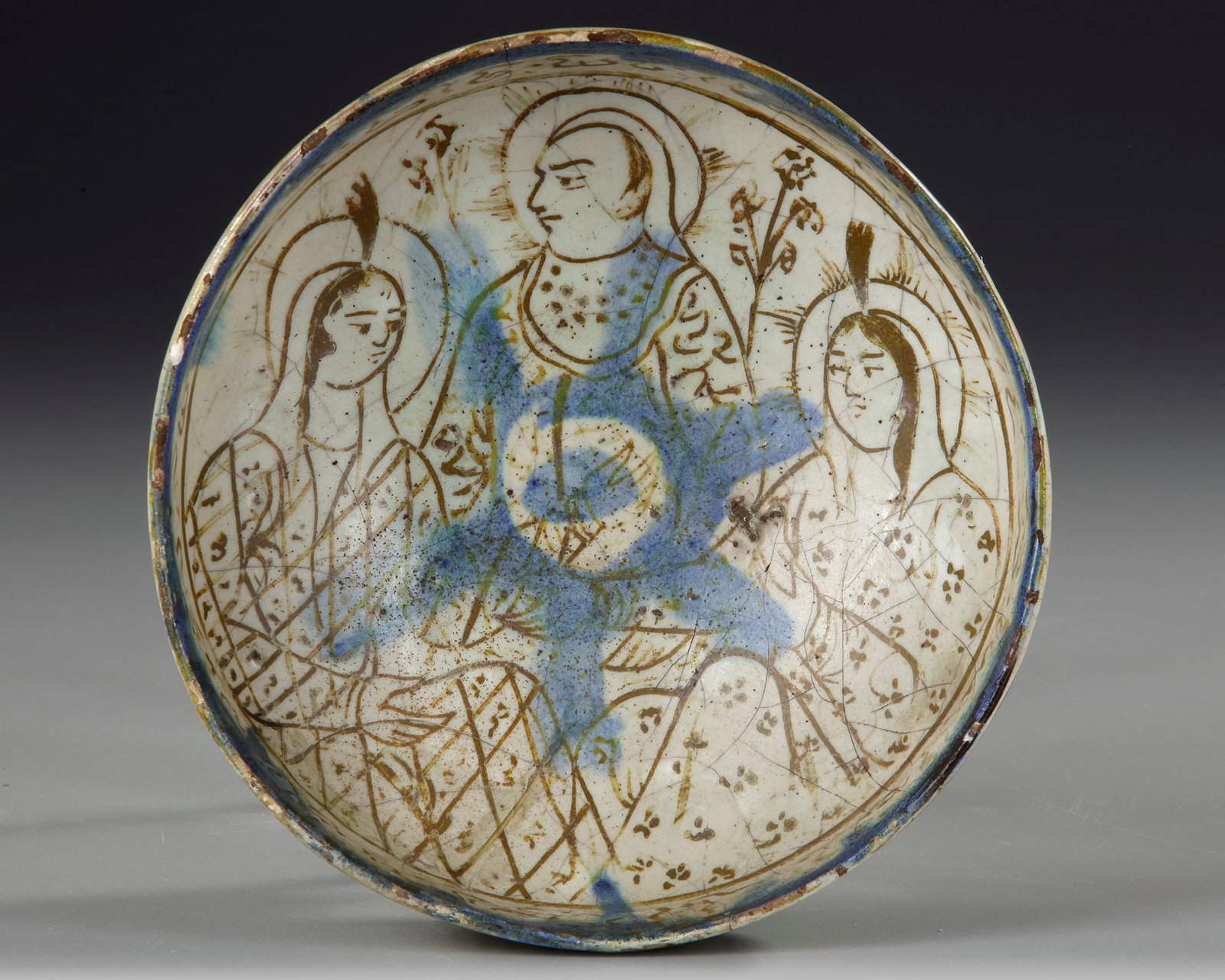 THREE-FIGURE BOWL, SELJUK PERIOD, PERSIA, 11TH CENTURY: A ceramic bowl with a carinated body and pedestal base, decorated in metallic lustre and cobalt blue. The interior shows a central male figure flanked by two haloed women, surrounded by a pseudo-epigr