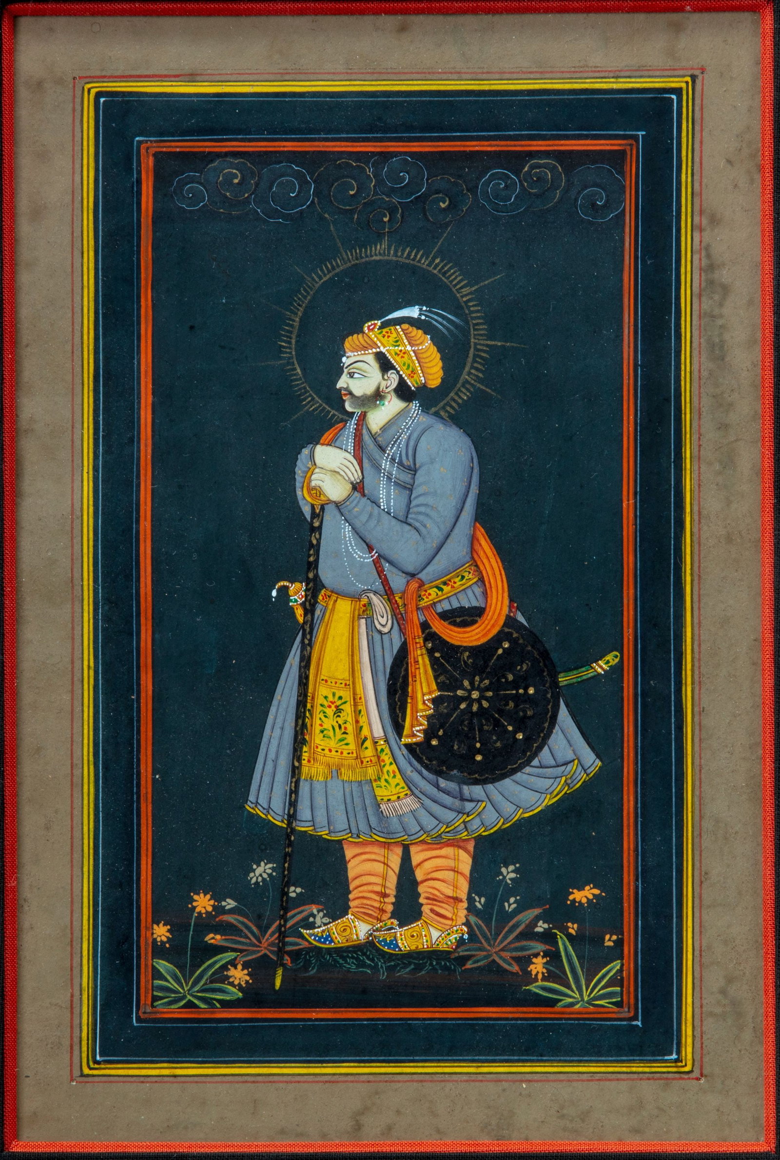 A MUGHAL MINIATURE OF A PRINCE, 19TH CENTURY: Gouache heightened with gold on paper, depicting a Mughal standing prince, wearing a jeweled red and gold turban, floral patka, holding a sword, a halo around his head, with a jeweled katar secured in