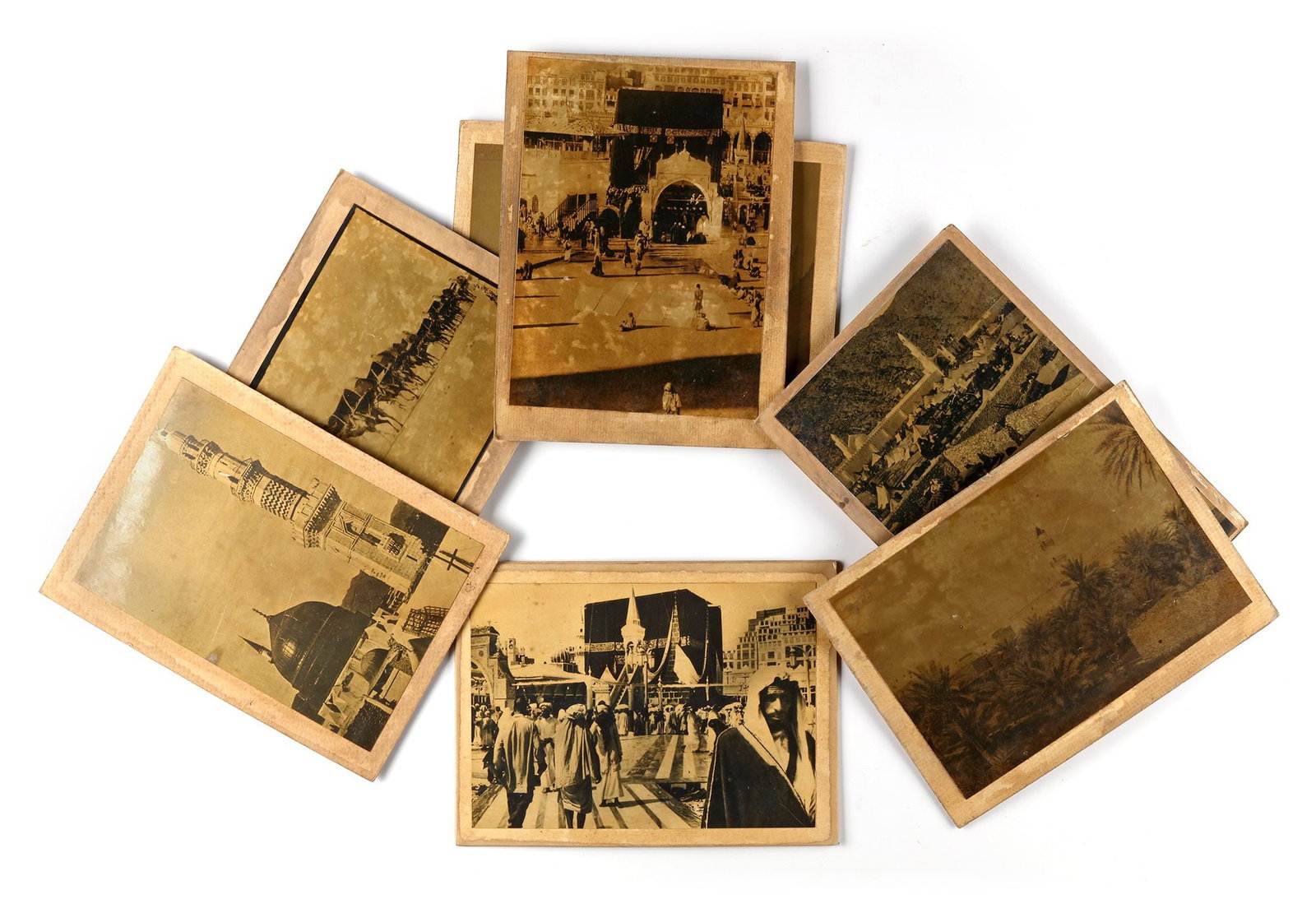 A COLLECTION OF SEVEN OLD PHOTOGRAPHS OF MECCA, MEDINA, THE MAHMAL AND THE HAJJ, EARLY 20TH CENTURY: Image of Mecca with prayers around the Kaaba, image of a bedouin caravan, two pictures of the pilgrim's tents at Muna. A view of Al-Baqi Cemetery, prayers going through al-Salam gate, a view of the ci