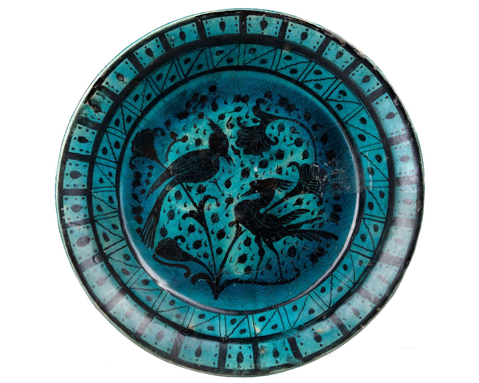 A RAQQA TURQUOISE-GLAZED POTTERY DISH, SYRIA, EARLY 13TH CENTURY: A pottery dish rising from short vertical foot through rounded body to everted rim, the interior painted in black under the glaze with a central roundel enclosing two elegant birds perched on a blosso